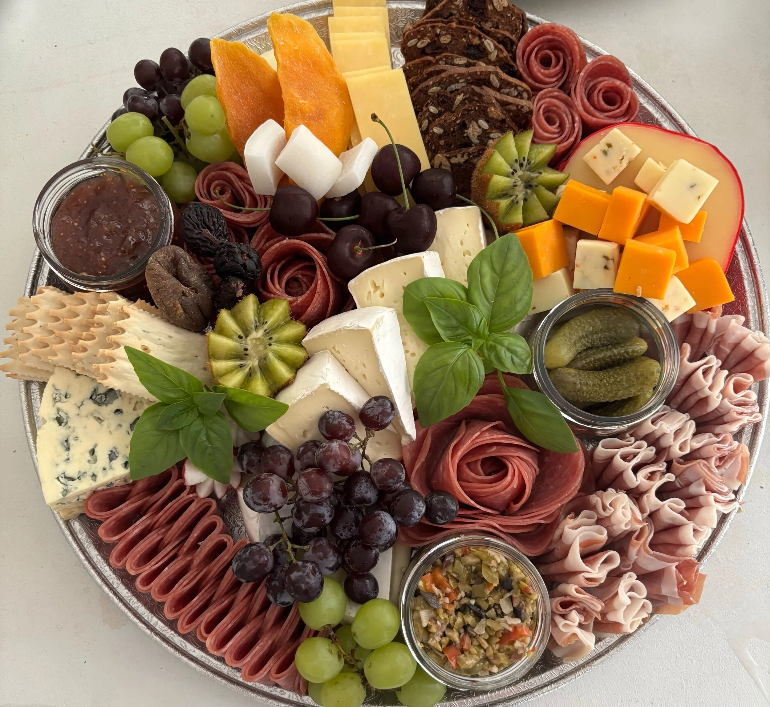 Charcuterie board with various cheeses, cured meats, fresh fruits, pickles, and garnishes.