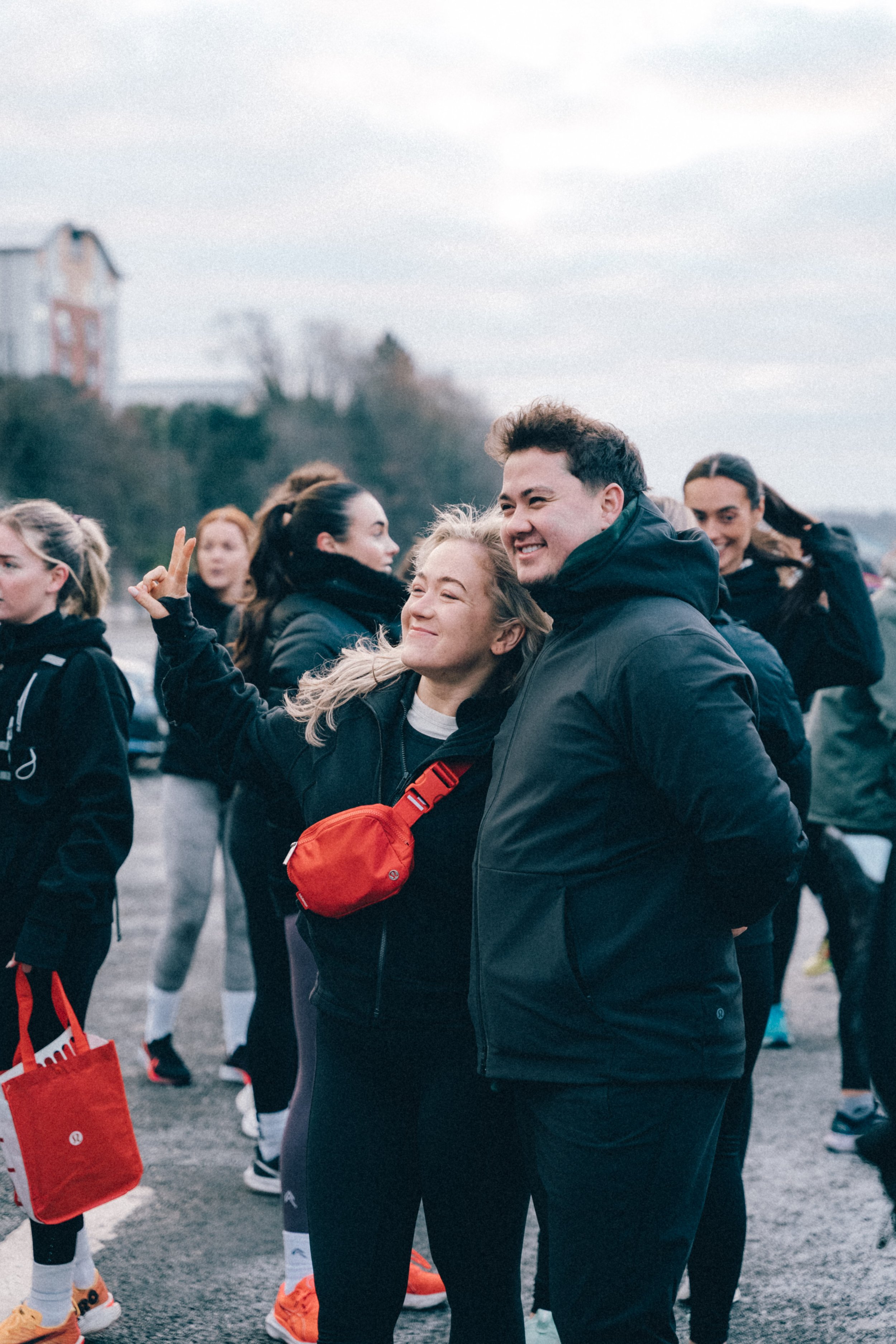 Group of smiling young people dressed in athletic clothing gathering outdoors, with two in the foreground posing happily for a photo.
