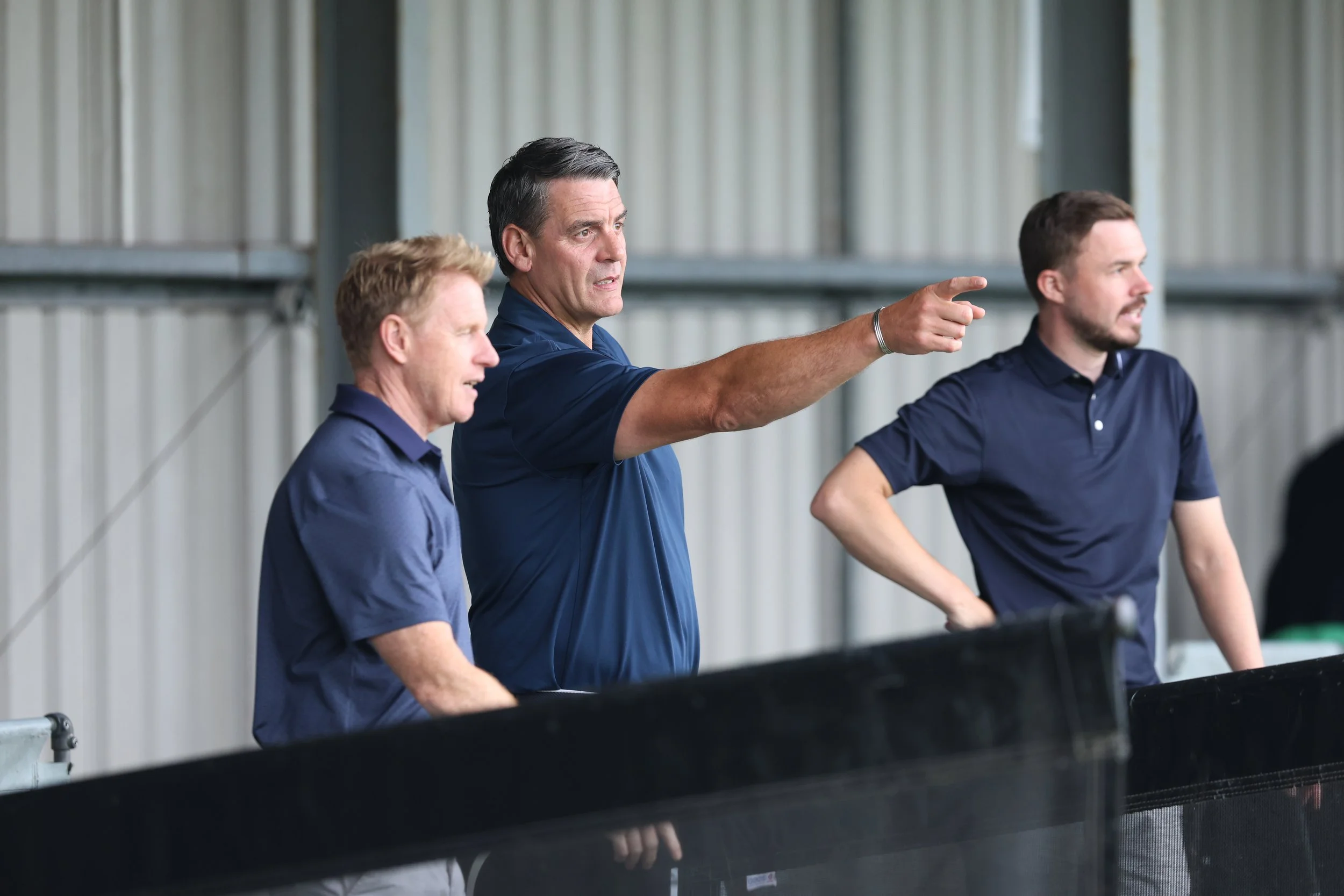 The Gowerton Golf Range Pro Team wearing navy shirts, standing in a bay and looking out onto the driving range