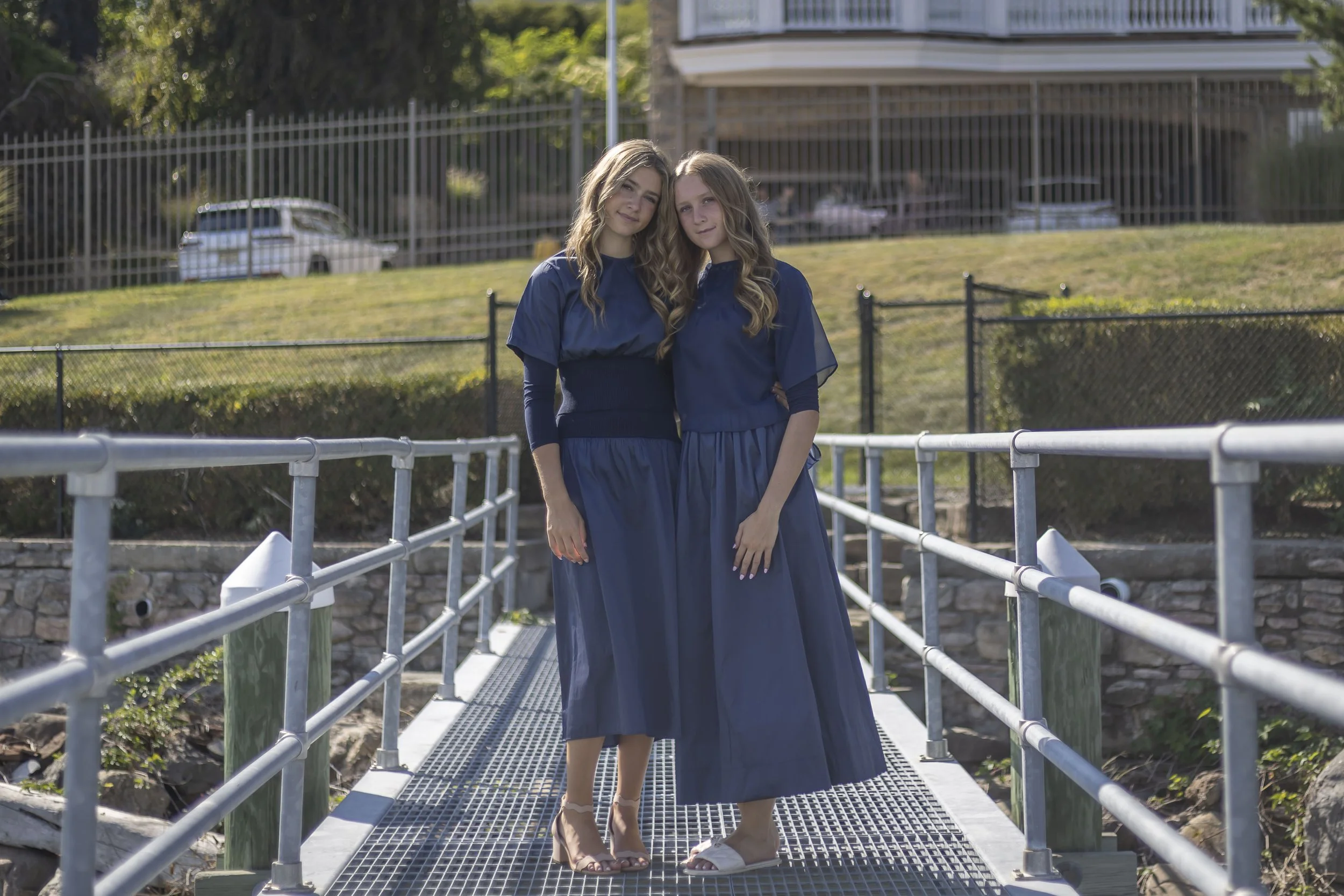 Four young women with long hair wearing vintage white and black dresses, standing on a marble staircase in an elegant building.