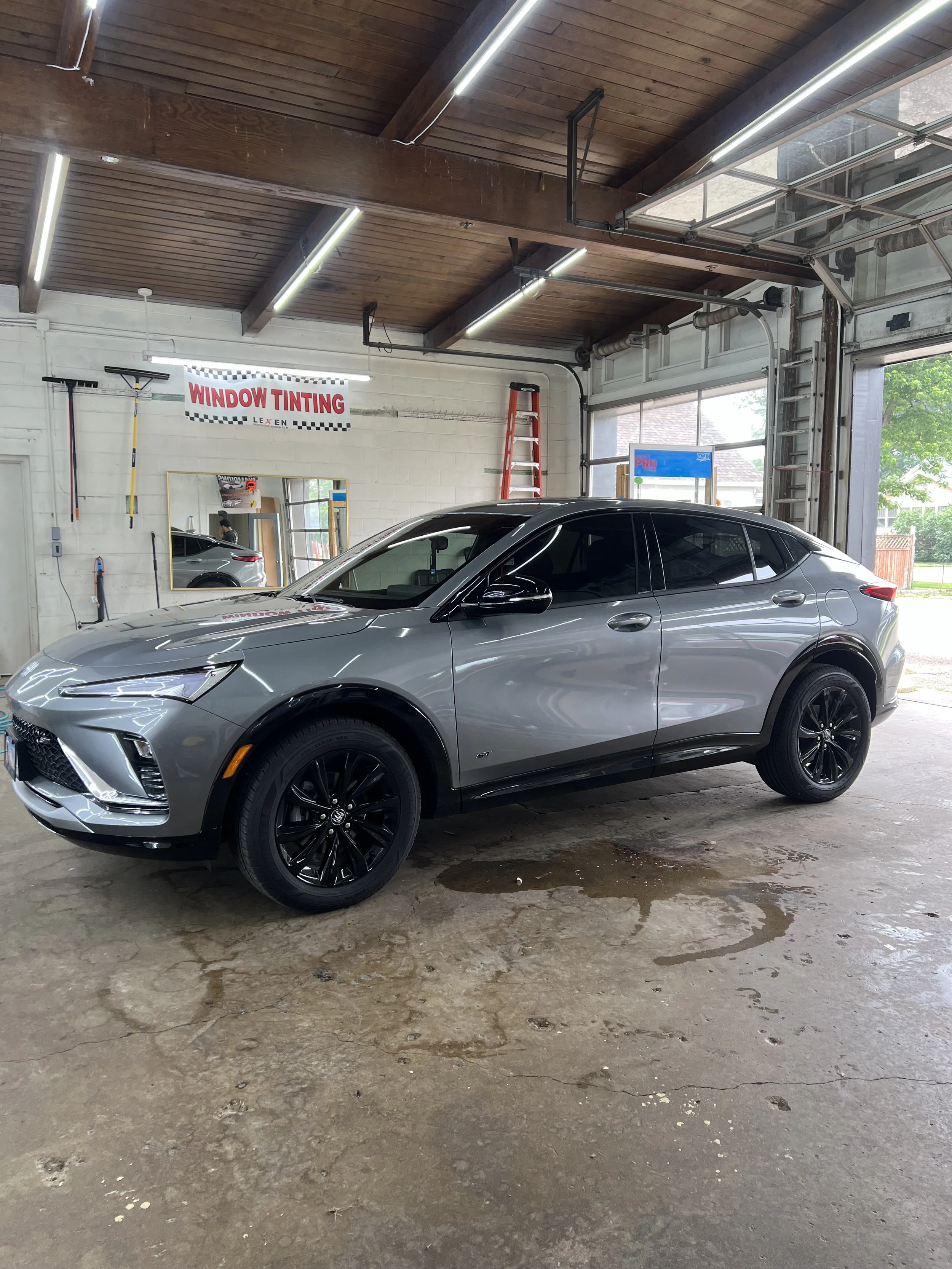 A silver SUV parked inside an automotive detailing shop with a sign that reads 'Window Tinting' in the background.