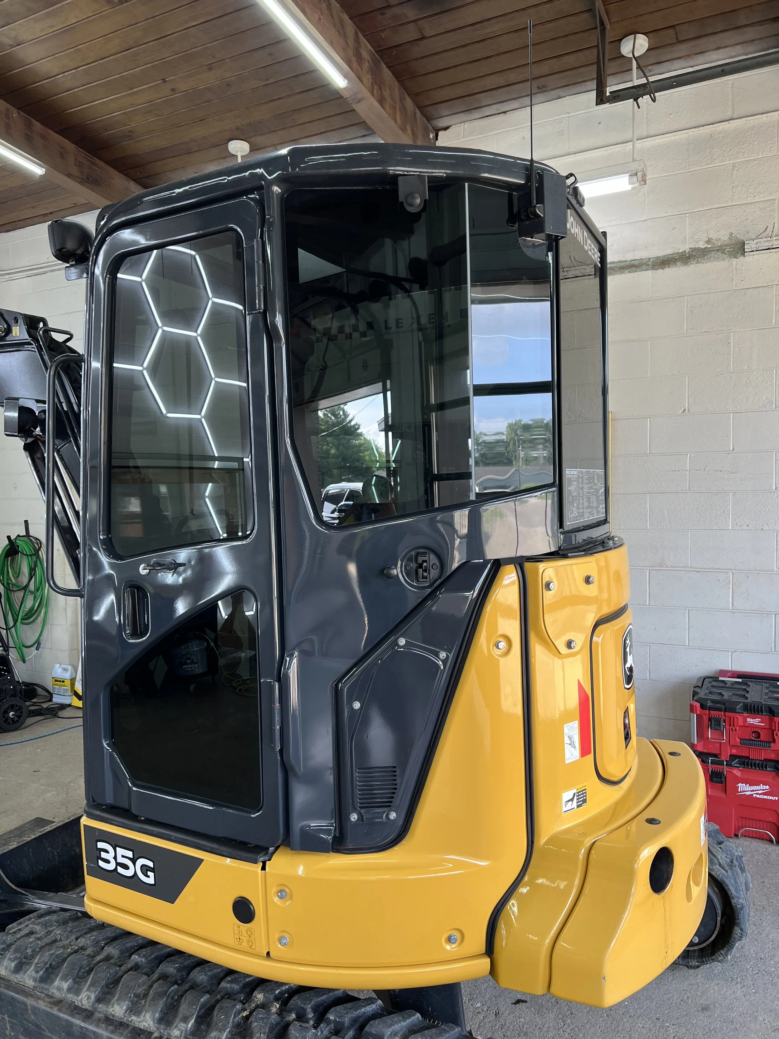 A yellow and black John Deere 35G compact excavator inside a garage.