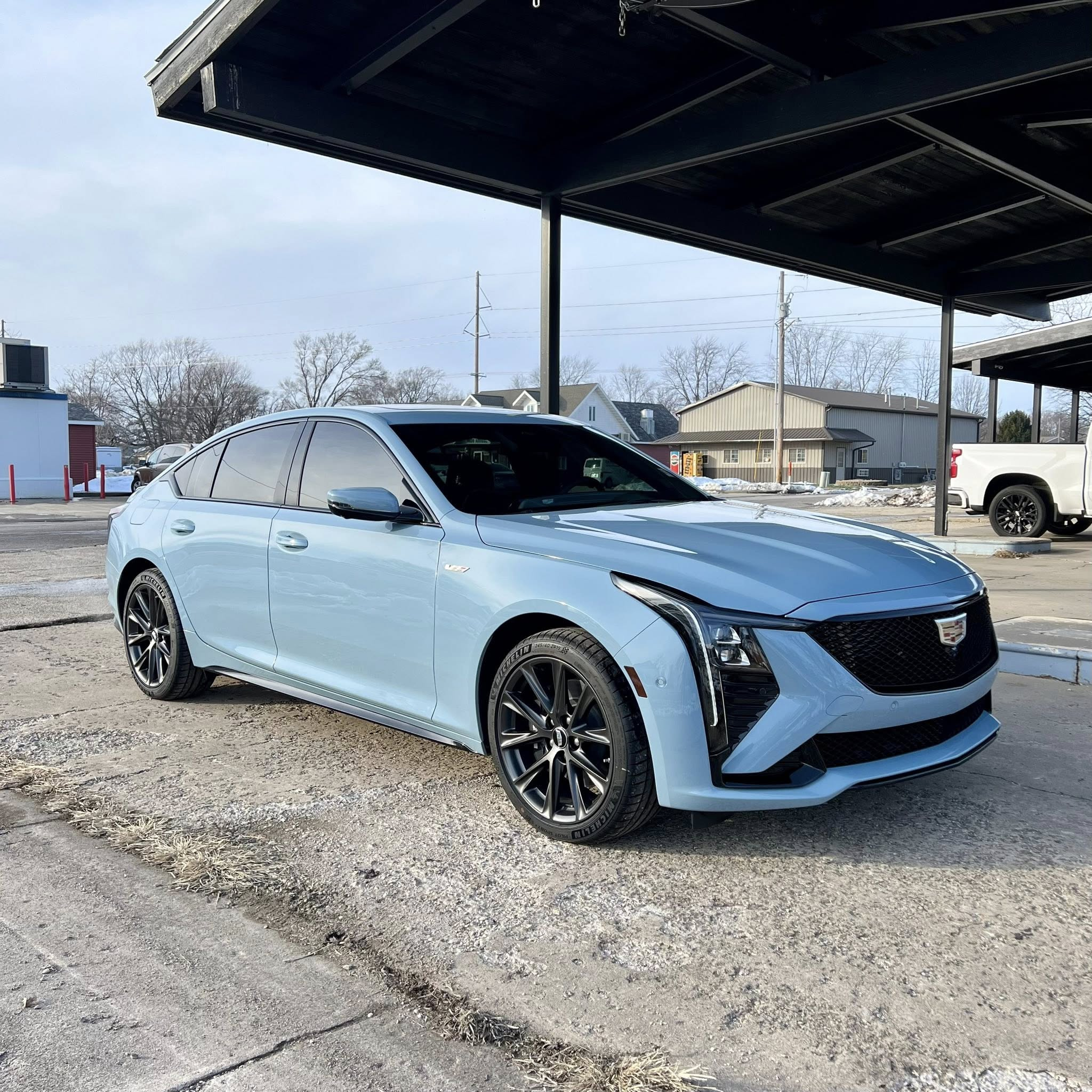 Light blue Cadillac sedan parked outdoors in a lot with other vehicles, under a shade structure.