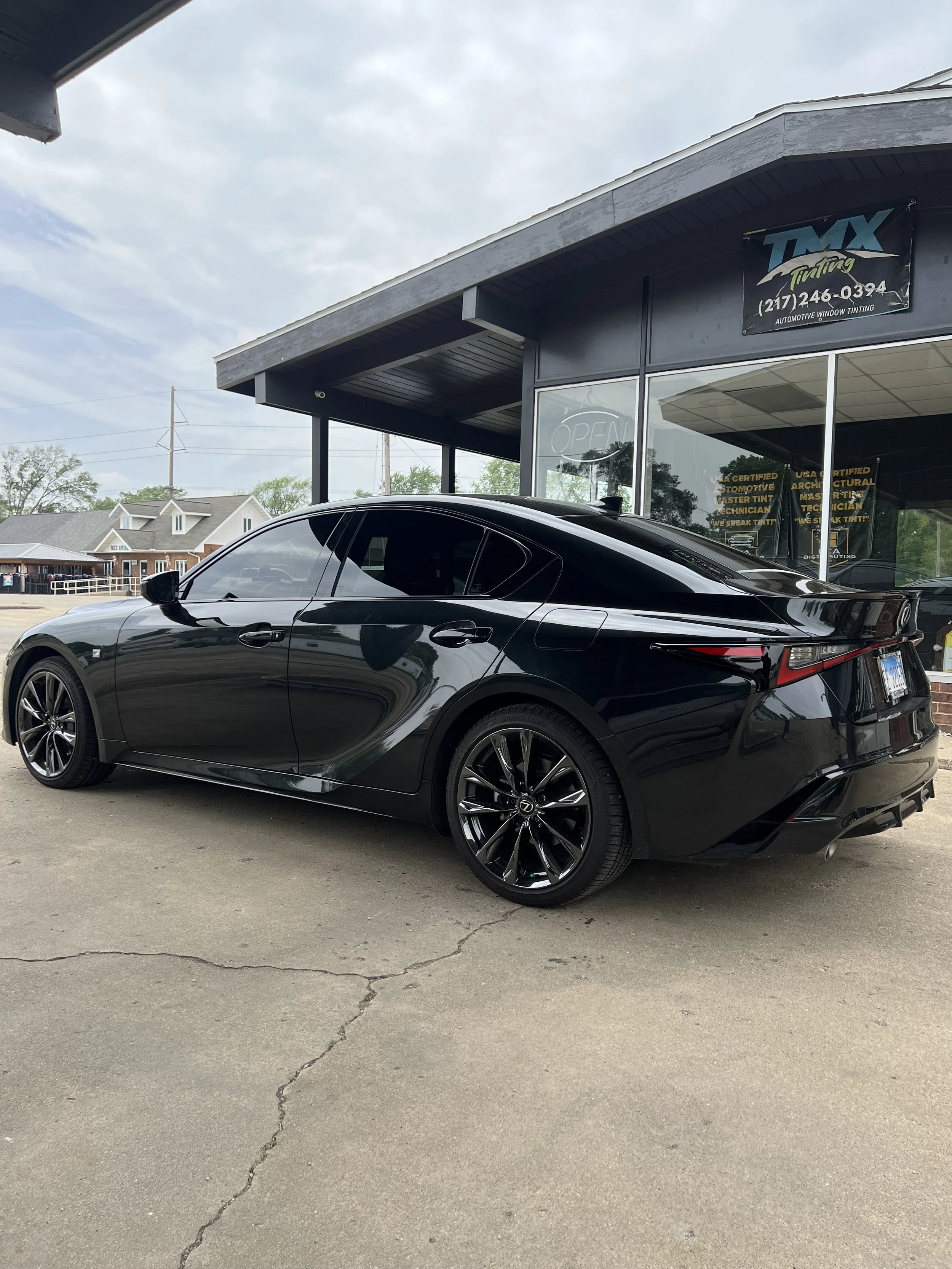 Black sedan car parked outside a building with signs advertising automotive window tinting and certification.