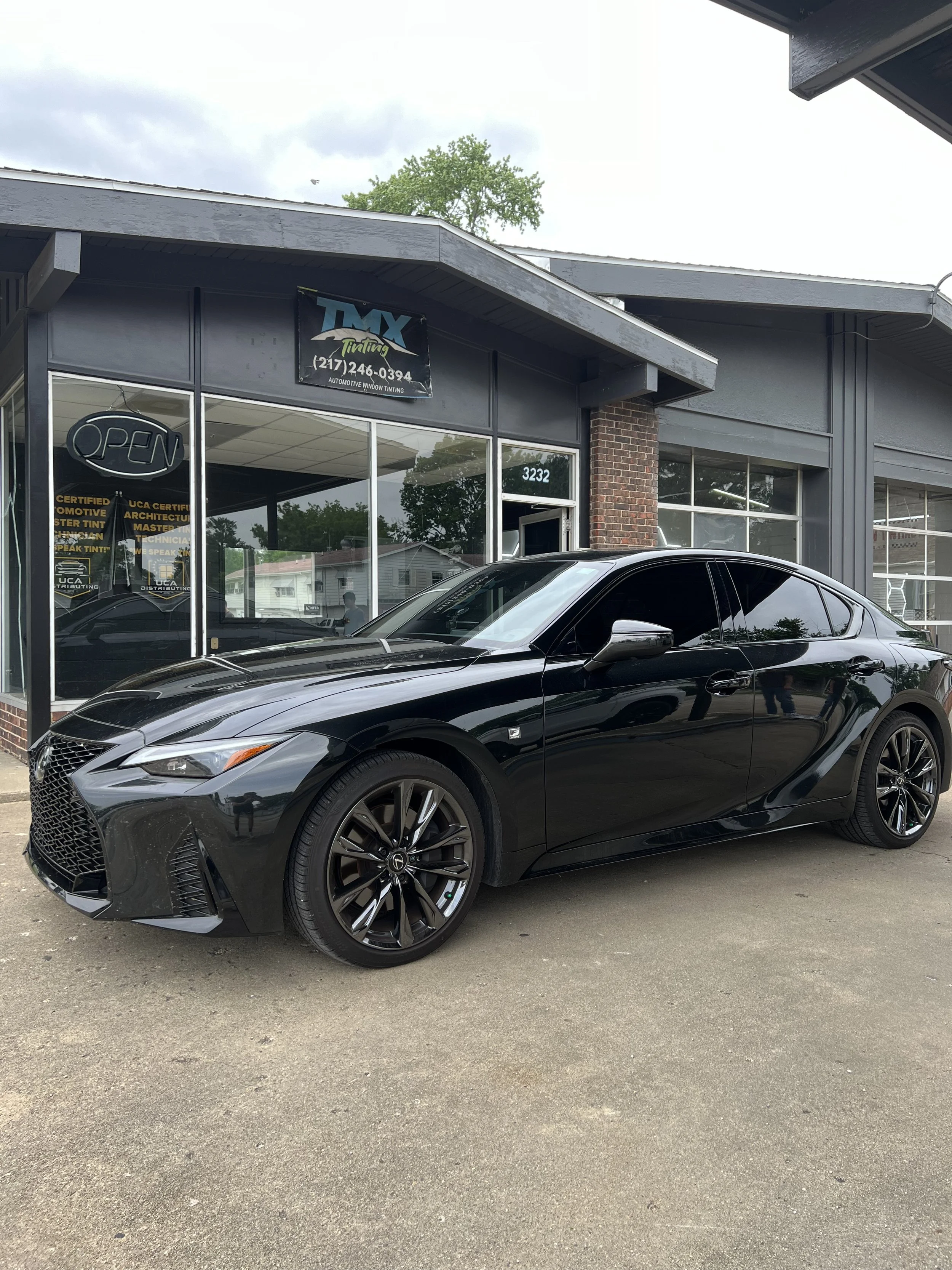 Black modern sedan parked outside a shop with large glass windows and a sign that reads 'TAX Tinting'.