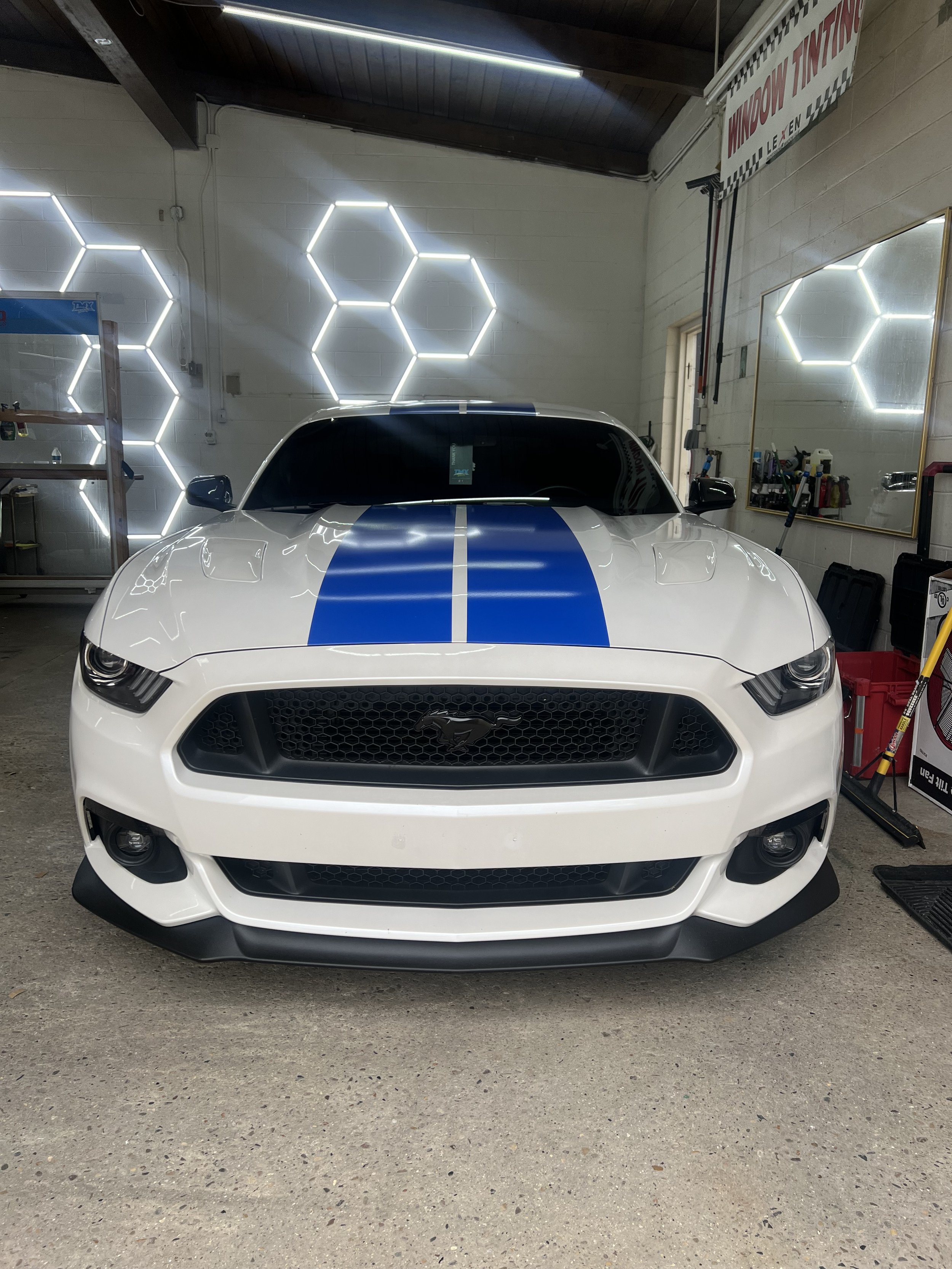 A white Ford Mustang with blue racing stripes parked inside a garage or workshop.
