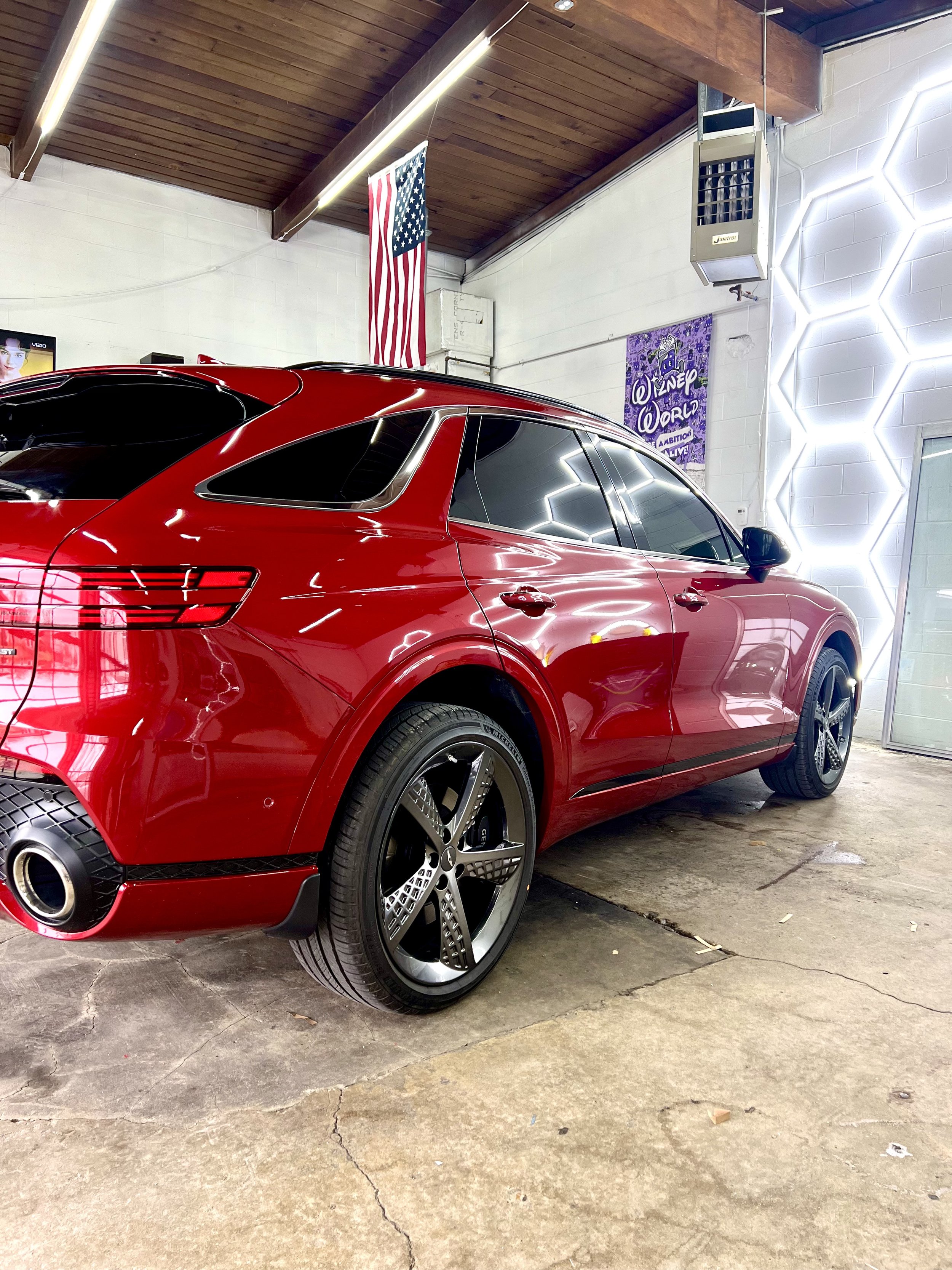 Red luxury SUV parked indoors with Wimbledon World poster, American flag, and illuminated wall decor in the background.