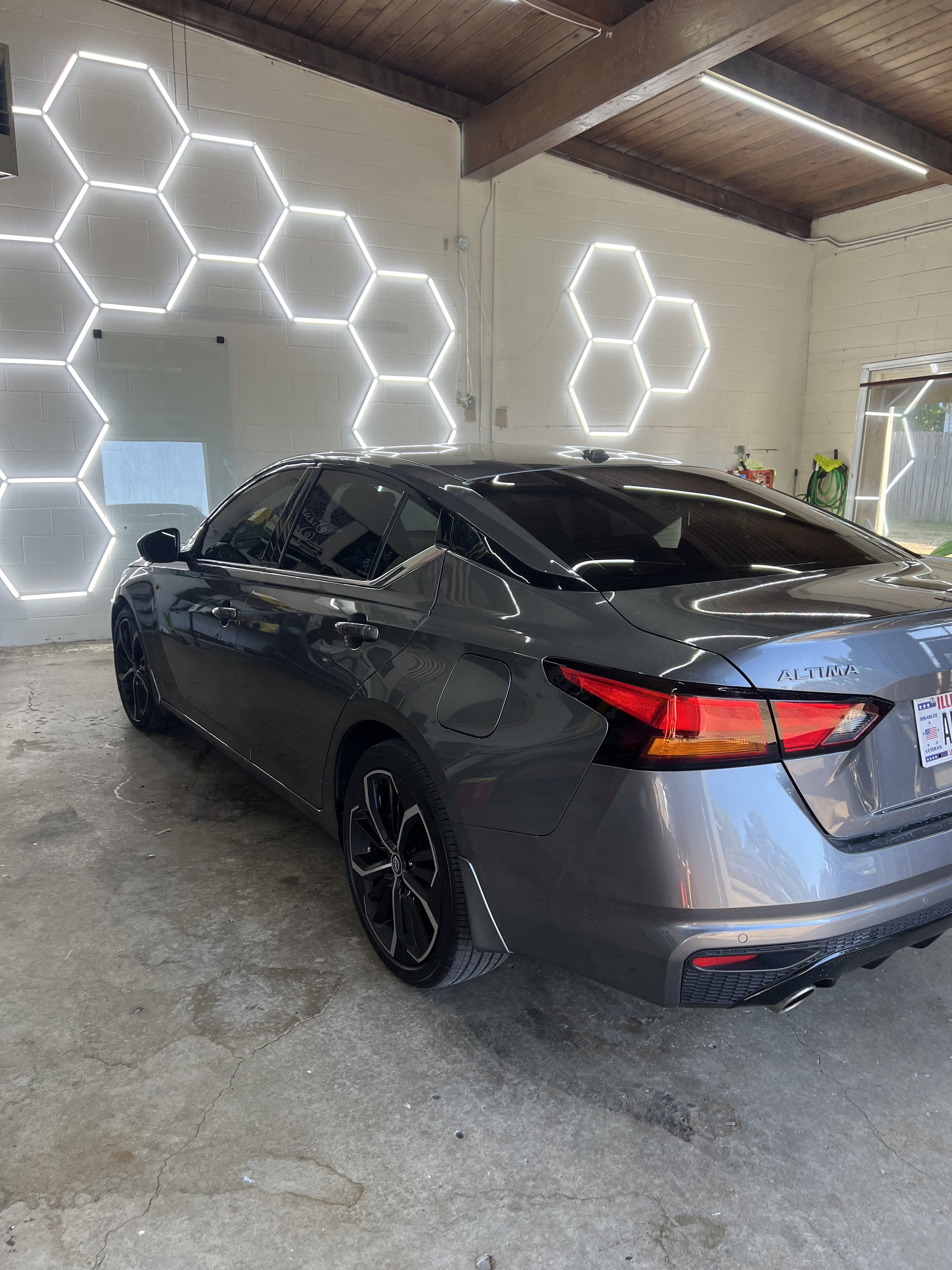 Gray Nissan Altima parked inside a garage with hexagonal LED light wall decor and concrete floors.