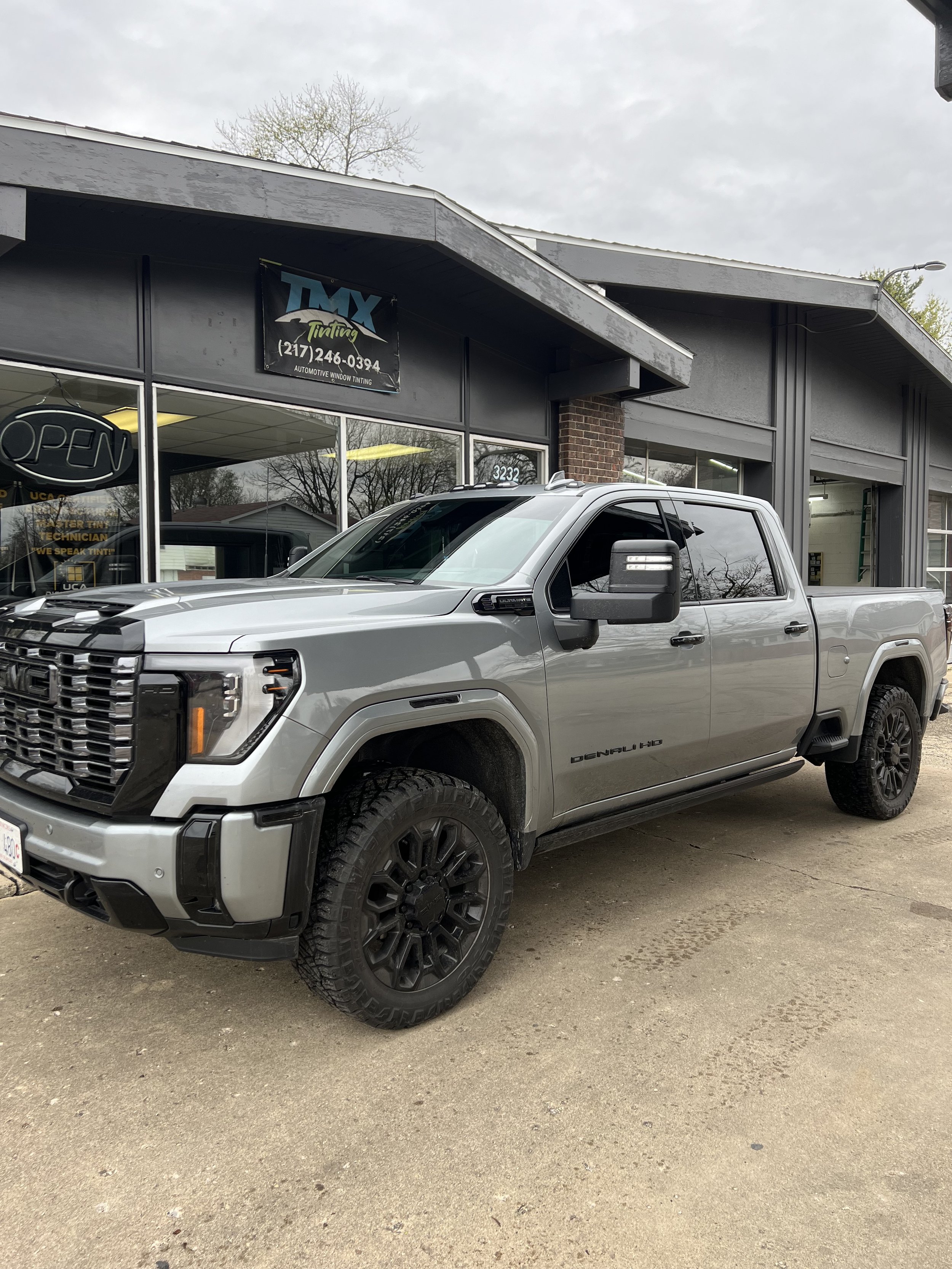 A silver GMC pickup truck parked outside an auto tinting shop with tinted windows and black wheels.