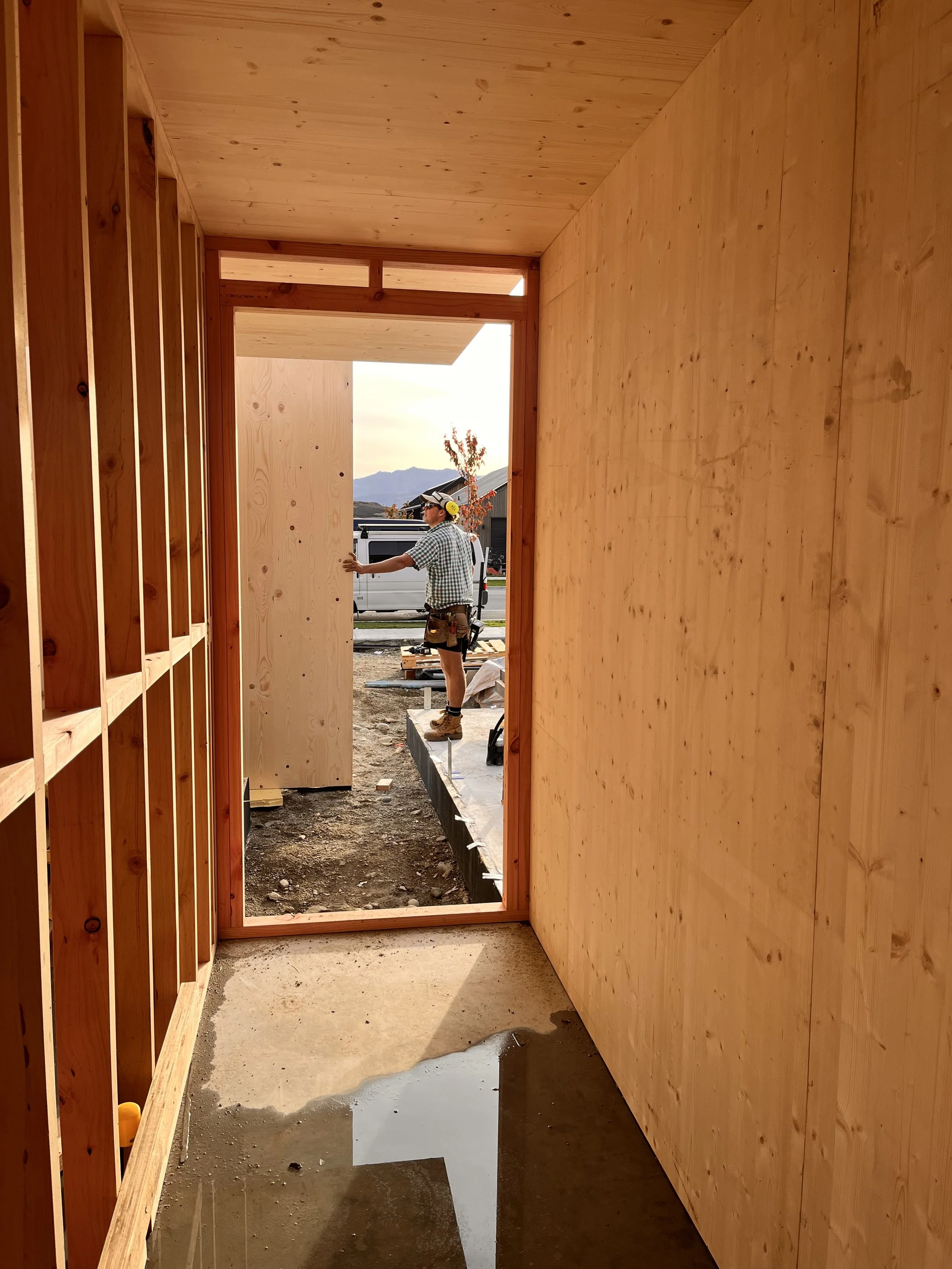 Wooden framing of a building under construction with a worker in a checked shirt and safety gear outside
