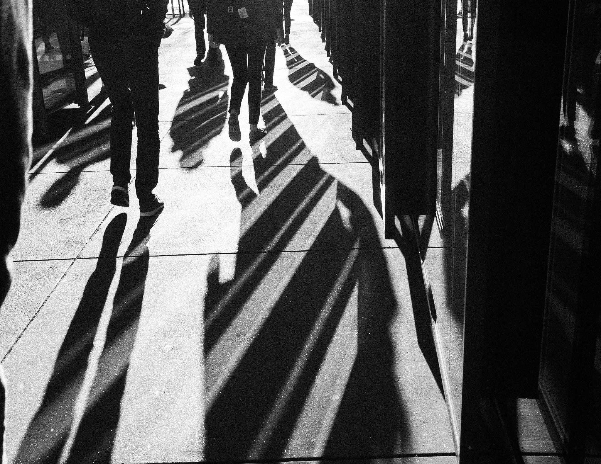 "Shadow Walk" Late light stretches city dwellers into silhouettes, their shadows weaving across pavement and glass. Legs in motion, forms blurred by reflection, this moment captures the city’s daily rhythm—anonymous, fleeting, and full of motion. In