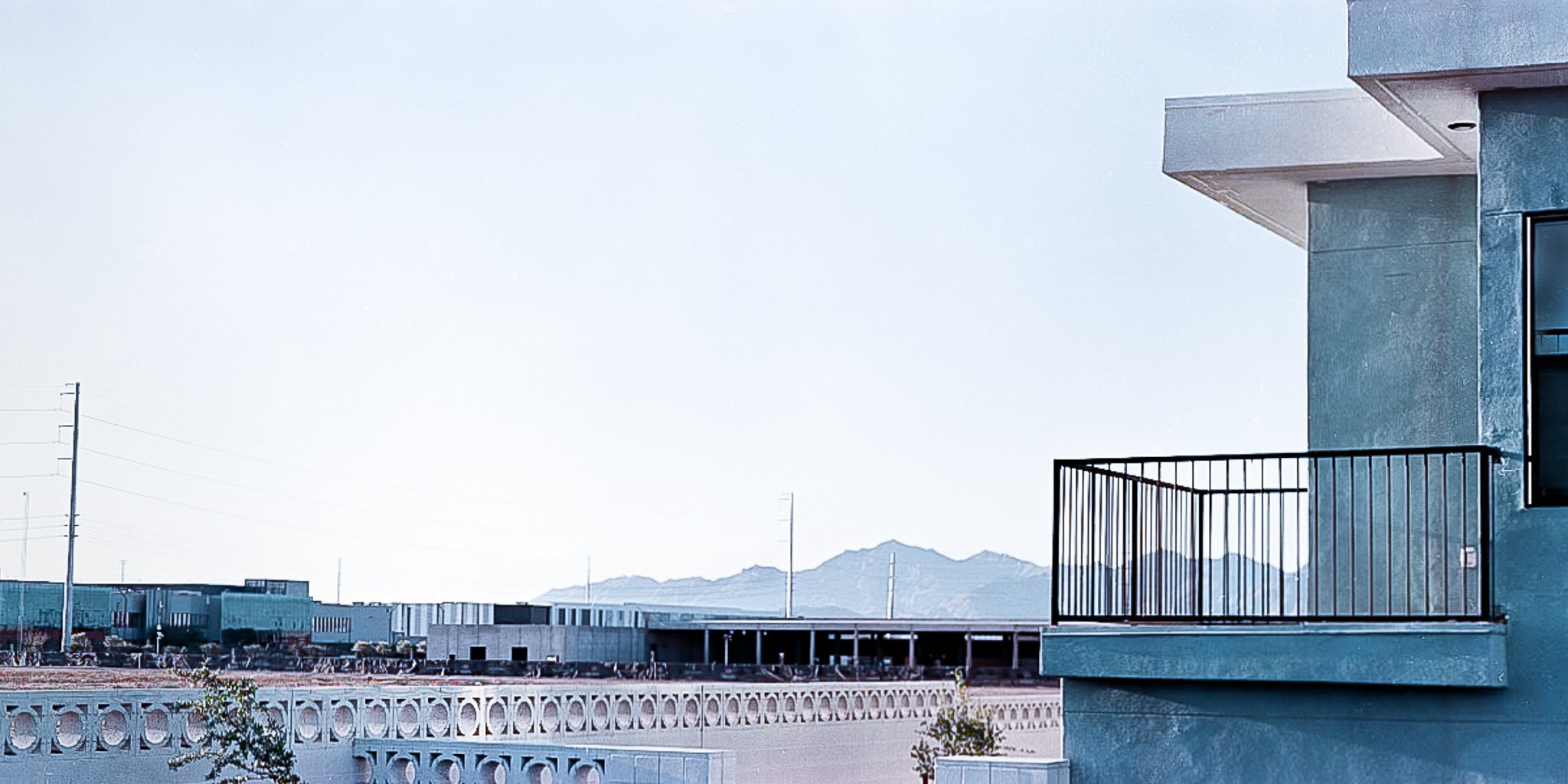 “Balcony View” From this vantage point, Estrella Mountain appears almost incidental—relegated to the distance behind construction sites. The clean geometry of the balcony in the foreground mirrors the repetitive barriers below, highlighting how even