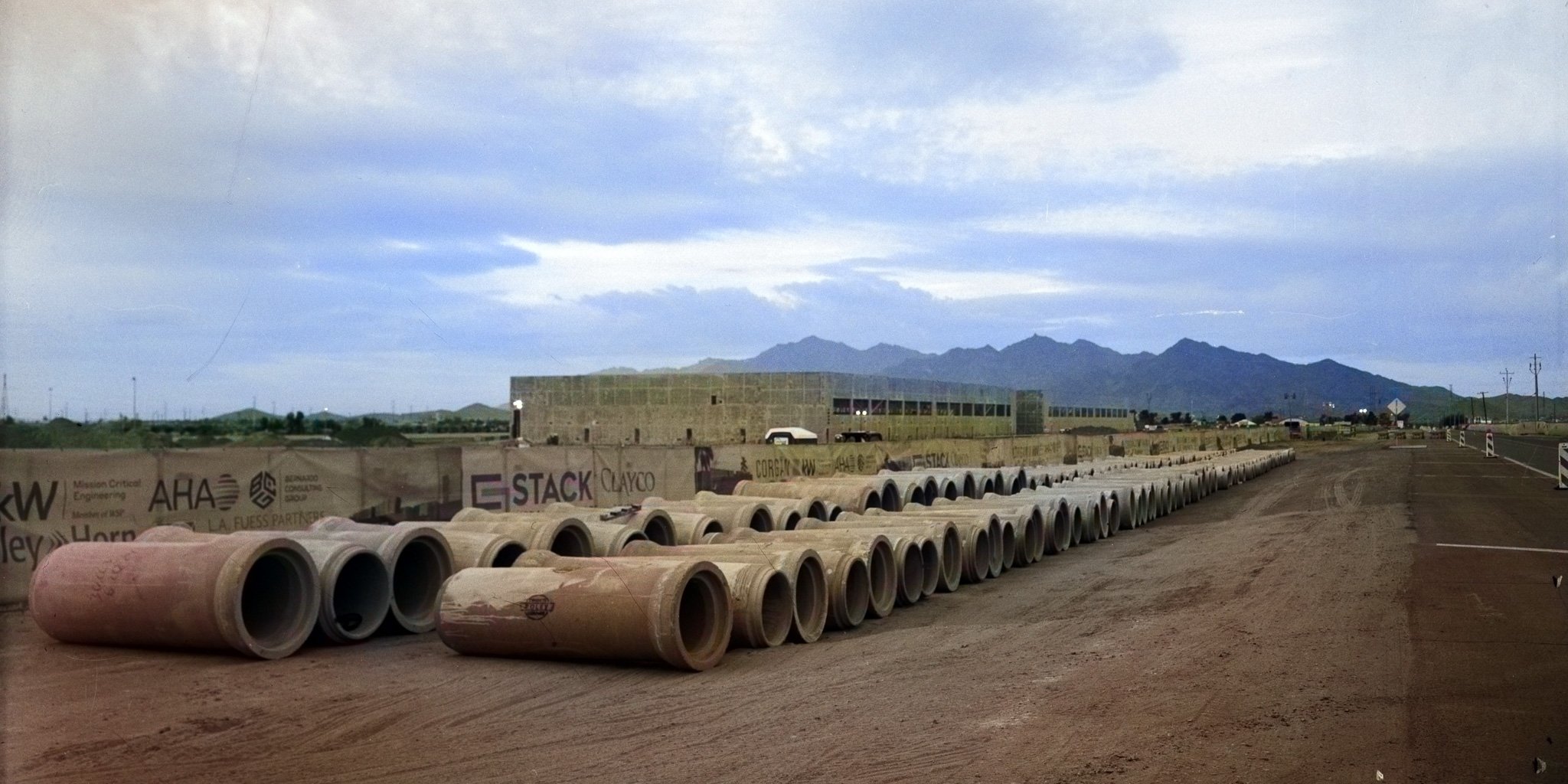 “Groundwork” Rows of concrete pipe stretch toward Estrella Mountain, forming a visual path that simultaneously leads to and away from the landscape beyond. The branded construction barriers and industrial materials assert ownership over the land, fra