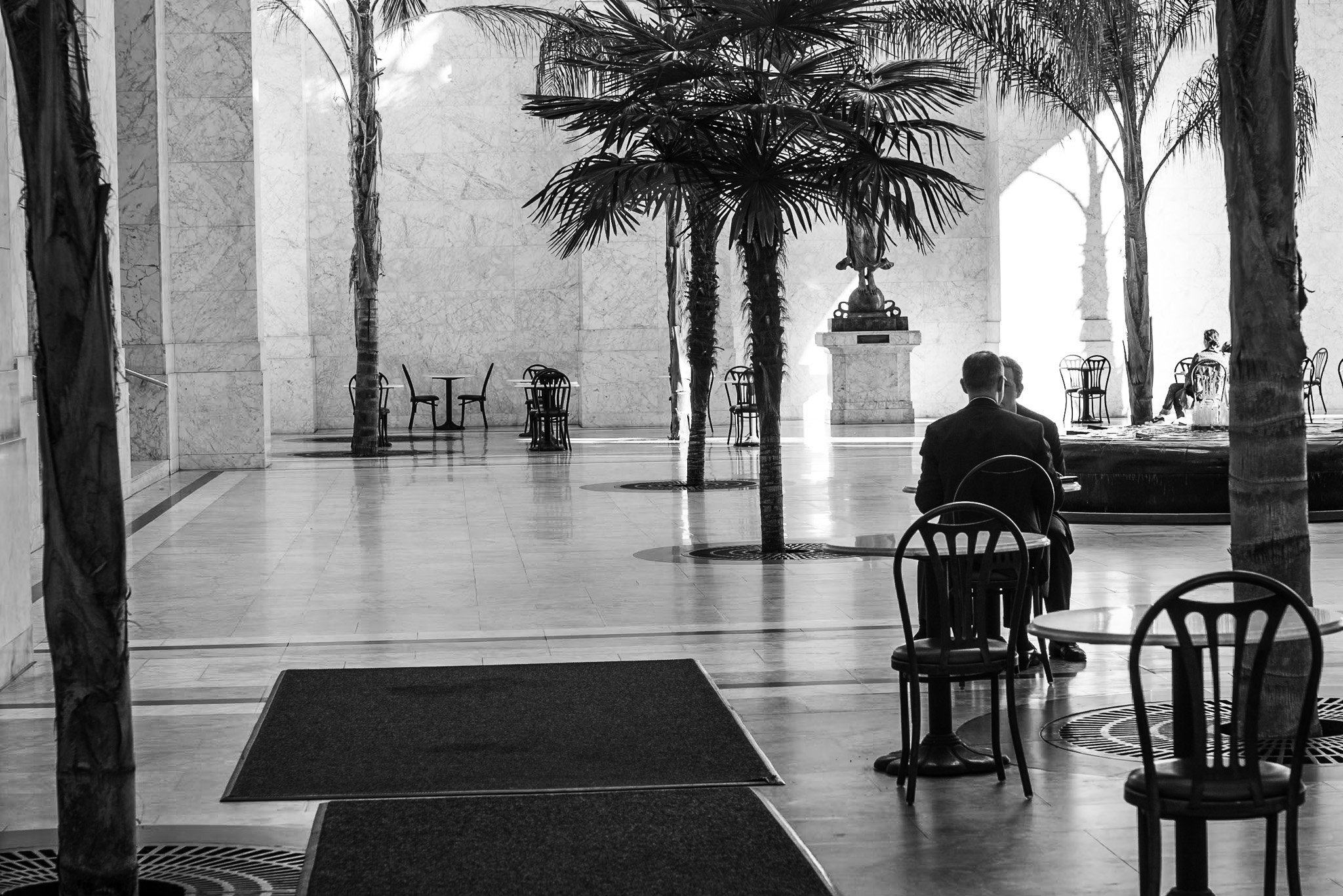 "Marble Silence"
In a sunlit atrium, two men talk quietly as others drift through the stillness. The space feels both civic and sacred—a pause from the rush outside. In The San Franciscans, even quiet corners hold the city’s voice, softened by light,