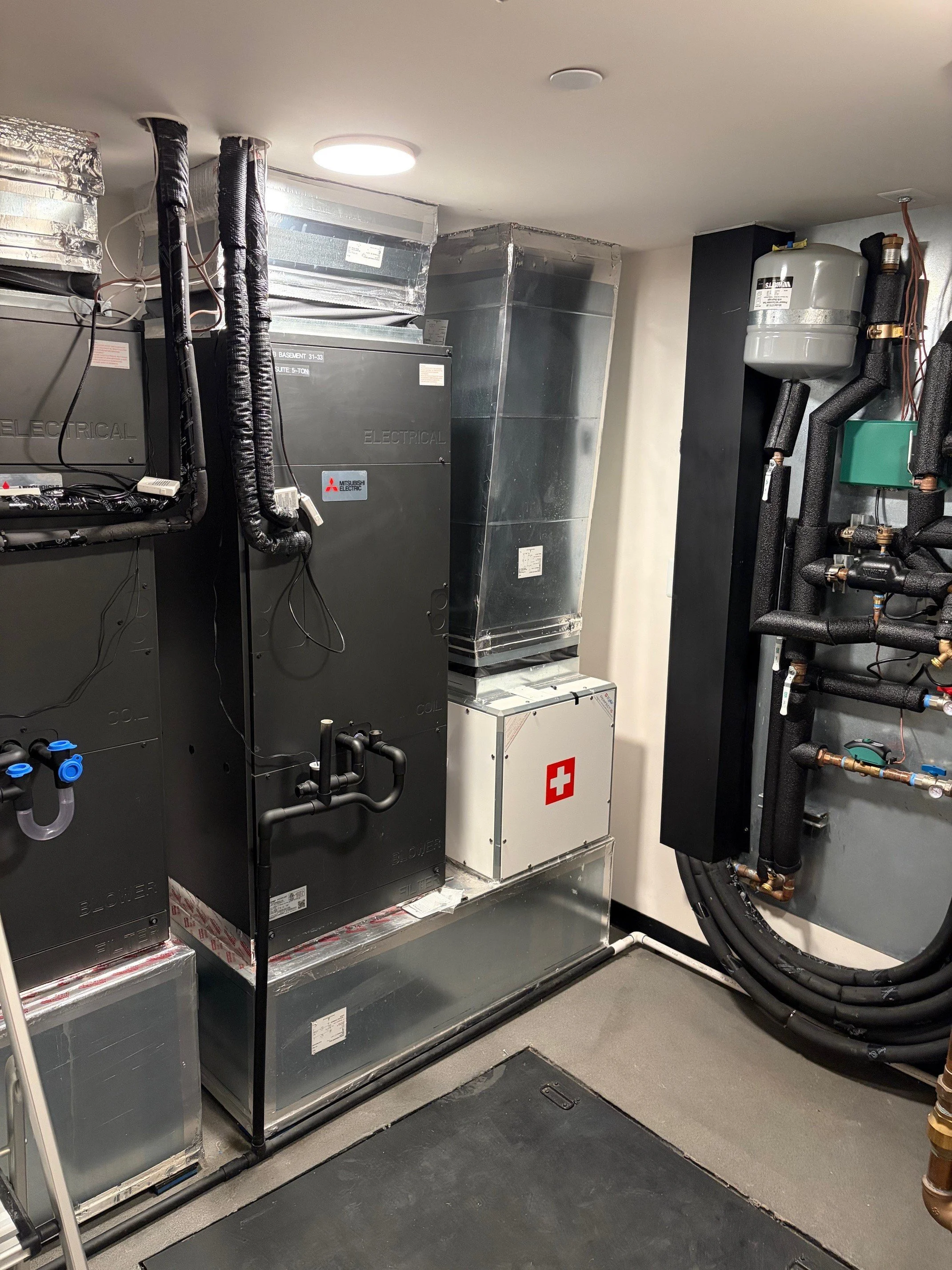 A mechanical room with air conditioning units and electrical equipment, including ductwork, refrigerant piping, and a Swiss HEPA filtration module.