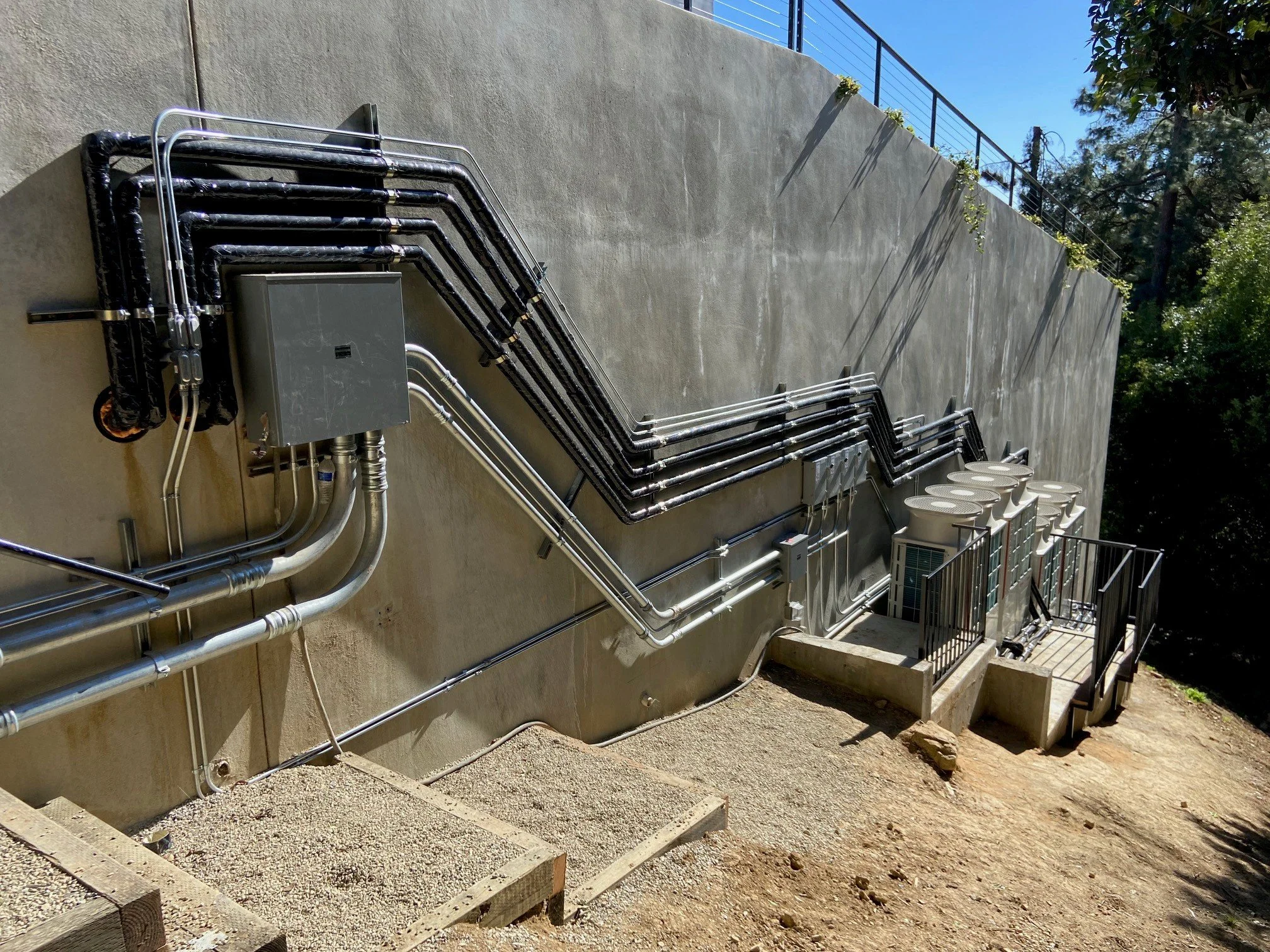 External view of HVAC units and electrical conduits attached to a concrete wall with stairs and handrails.