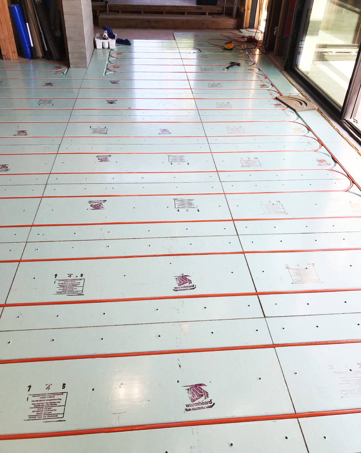 Installing underfloor heating with heat mats in a room with large windows and sliding glass door. Tools and wiring visible.