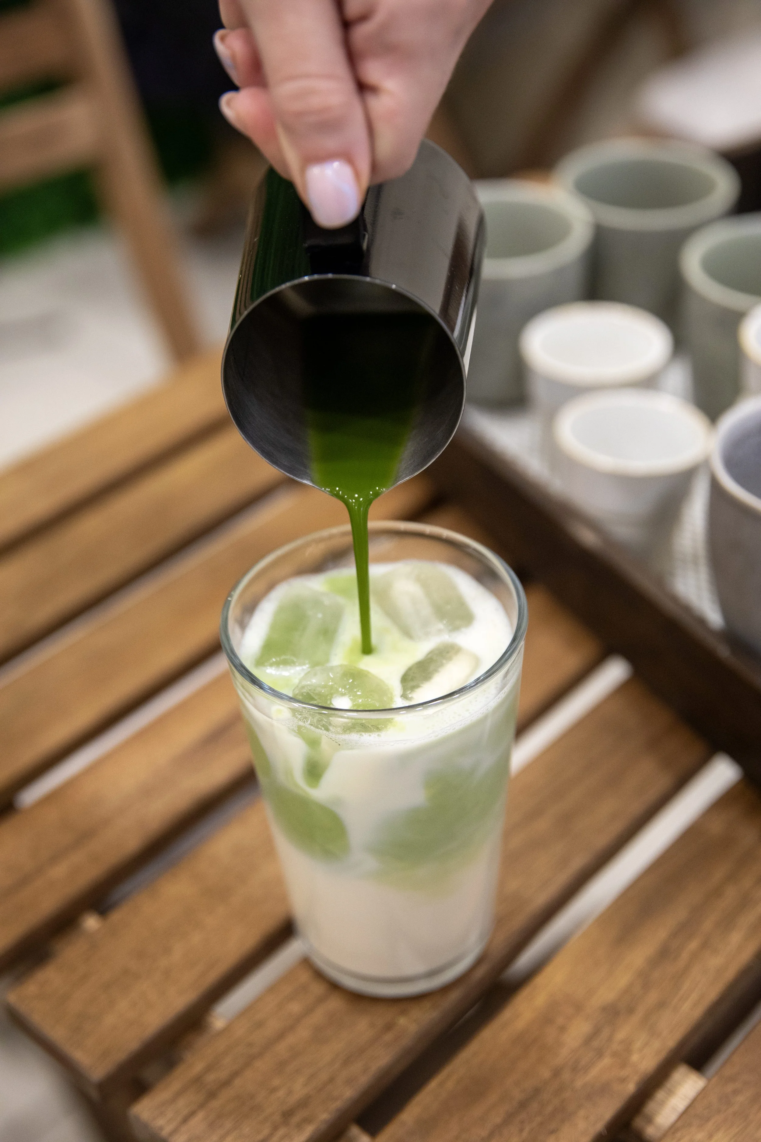 A hand pouring green syrup into a glass of milk and ice with lime slices.