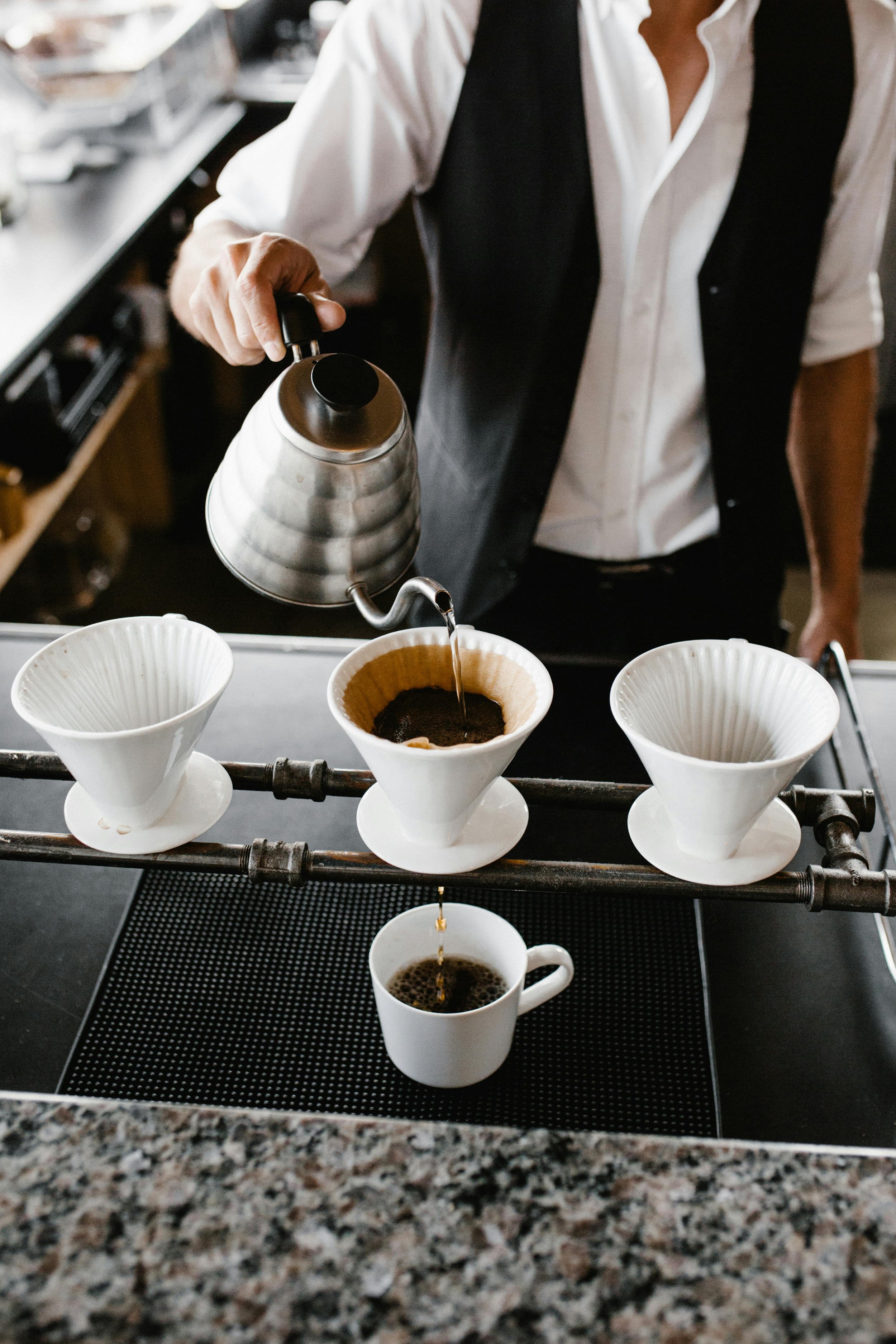 A barista pours hot water into coffee filters to brew pour-over coffee in a cafe.