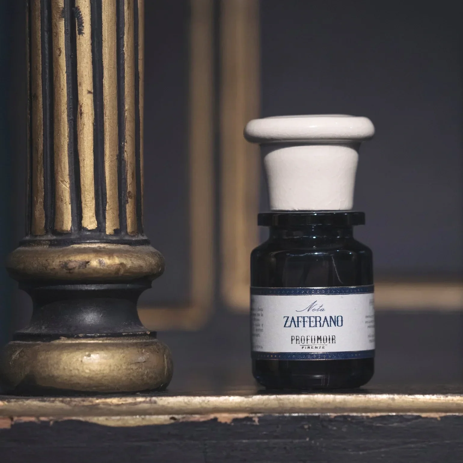 Close-up of an antique wooden candlestick holder and a small bottle of Zafferano Profumo perfume on a rustic shelf.