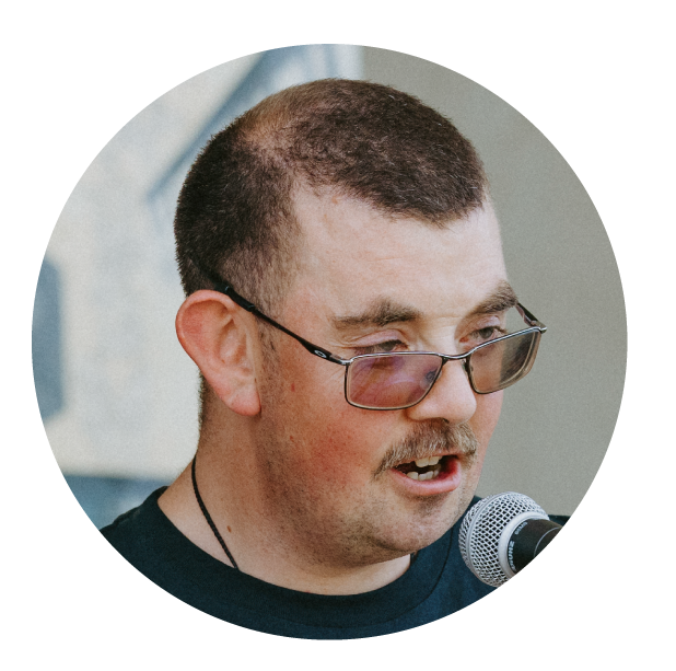 A man with short haircut, glasses, and a mustache speaking into a microphone.