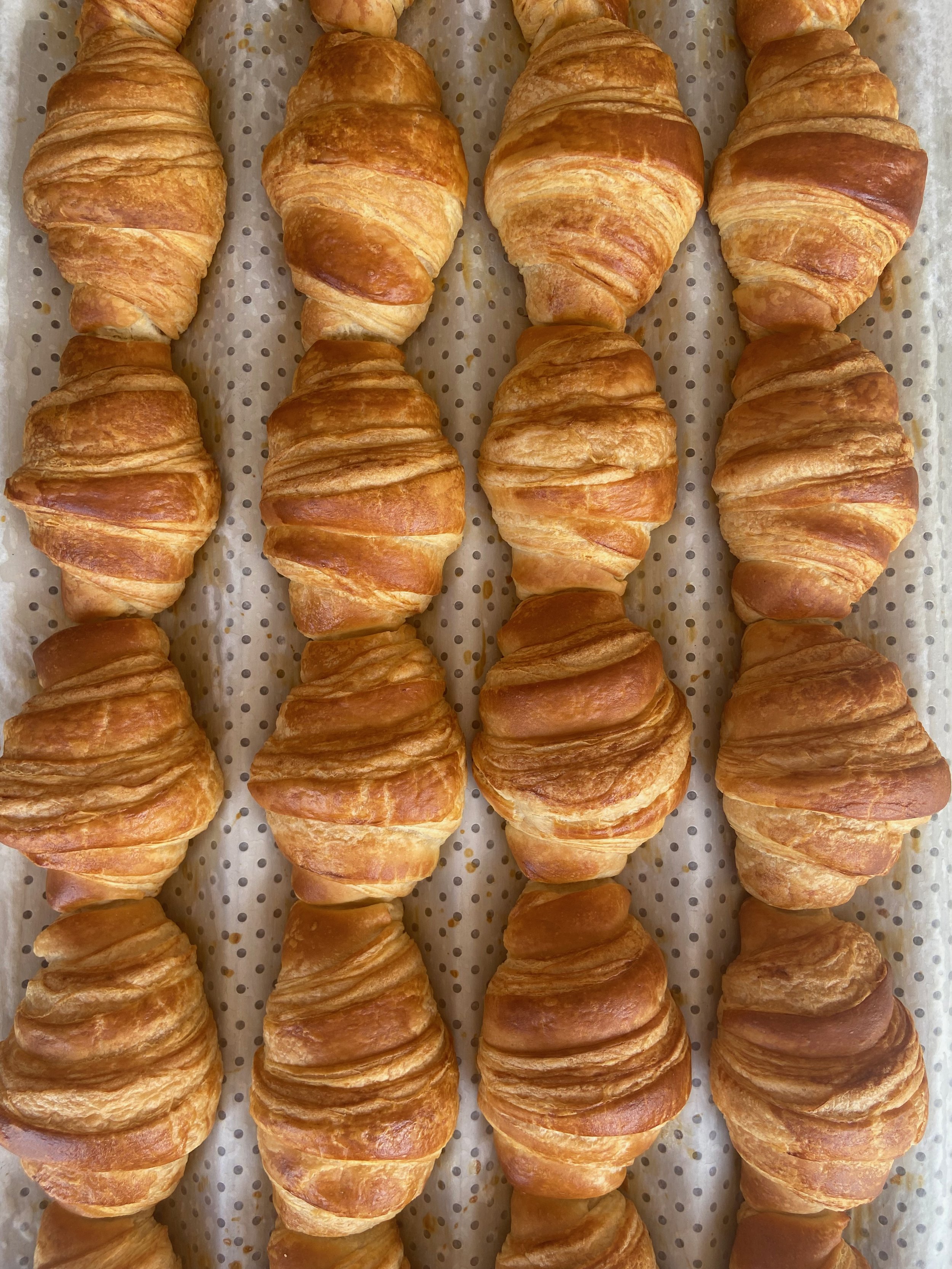 A tray of fresh, golden-brown croissants on parchment paper.