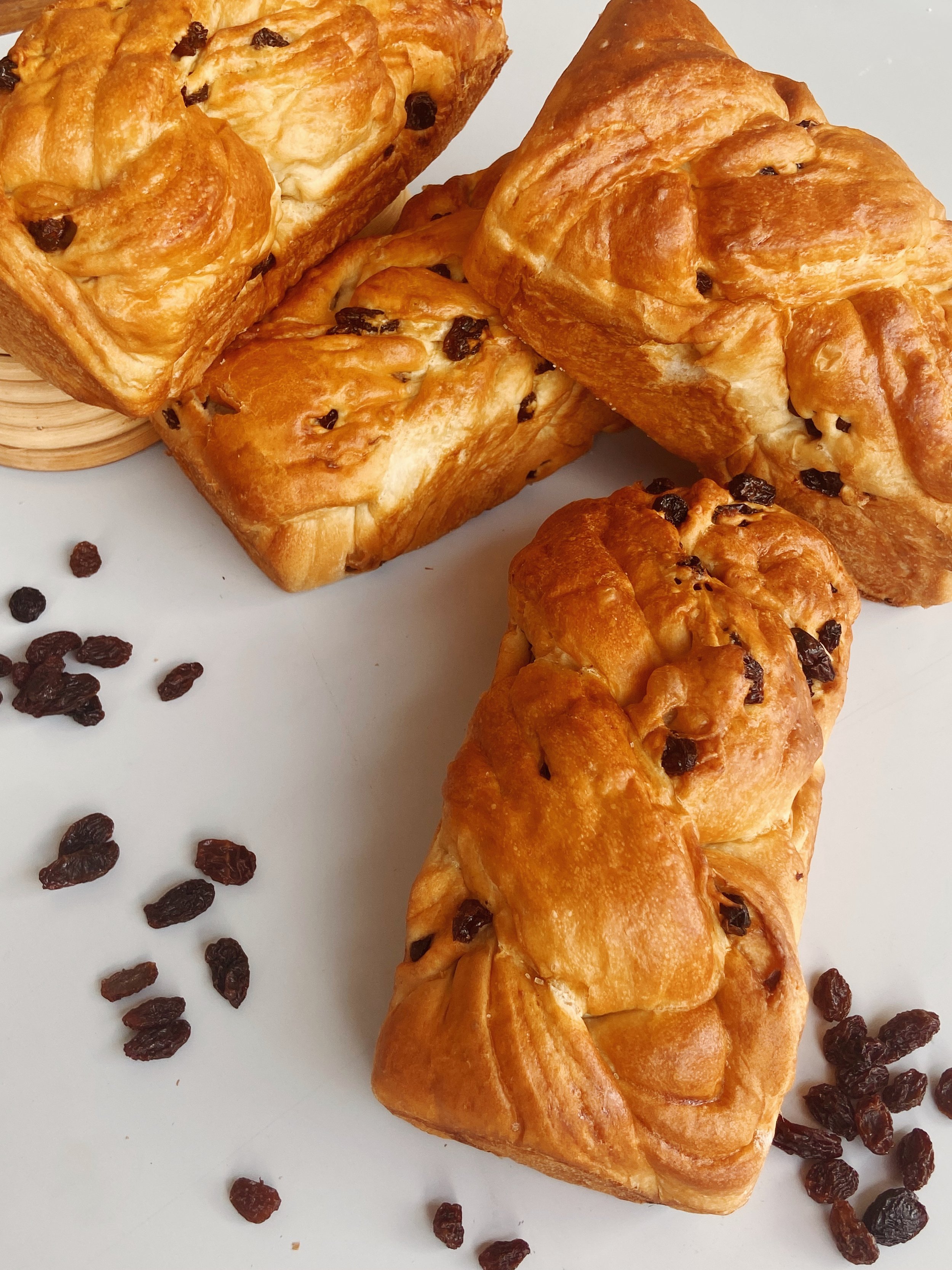 Three raisin Danish pastries and scattered raisins on a white surface.