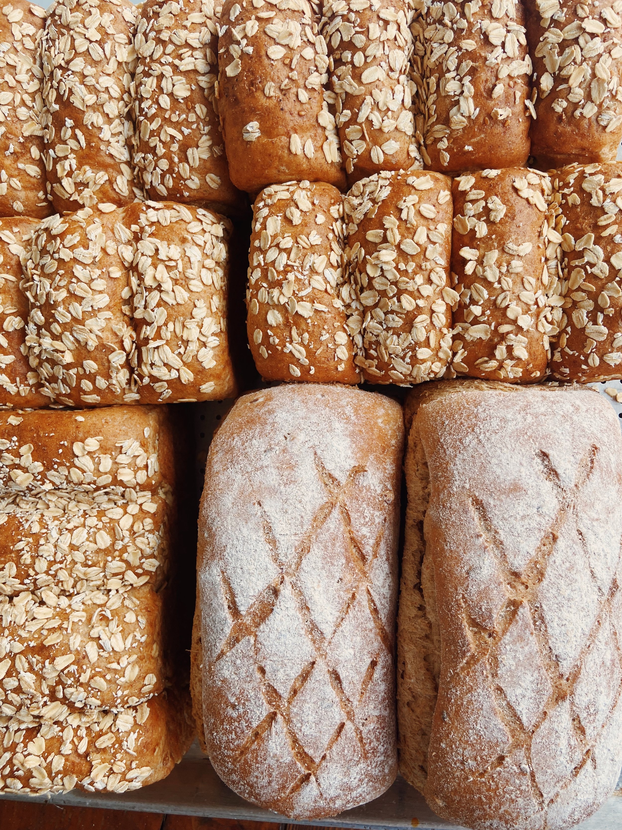 A display of various types of bread, including topped rolls with oats and sliced loaves with decorative scoring.