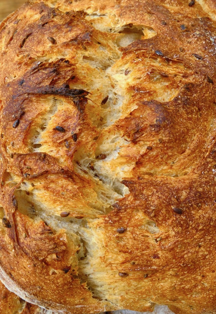 Close-up of a freshly baked loaf of bread with a golden-brown crust, some cracks, and seeds on top. from best bakary in panama, Pan y Canela