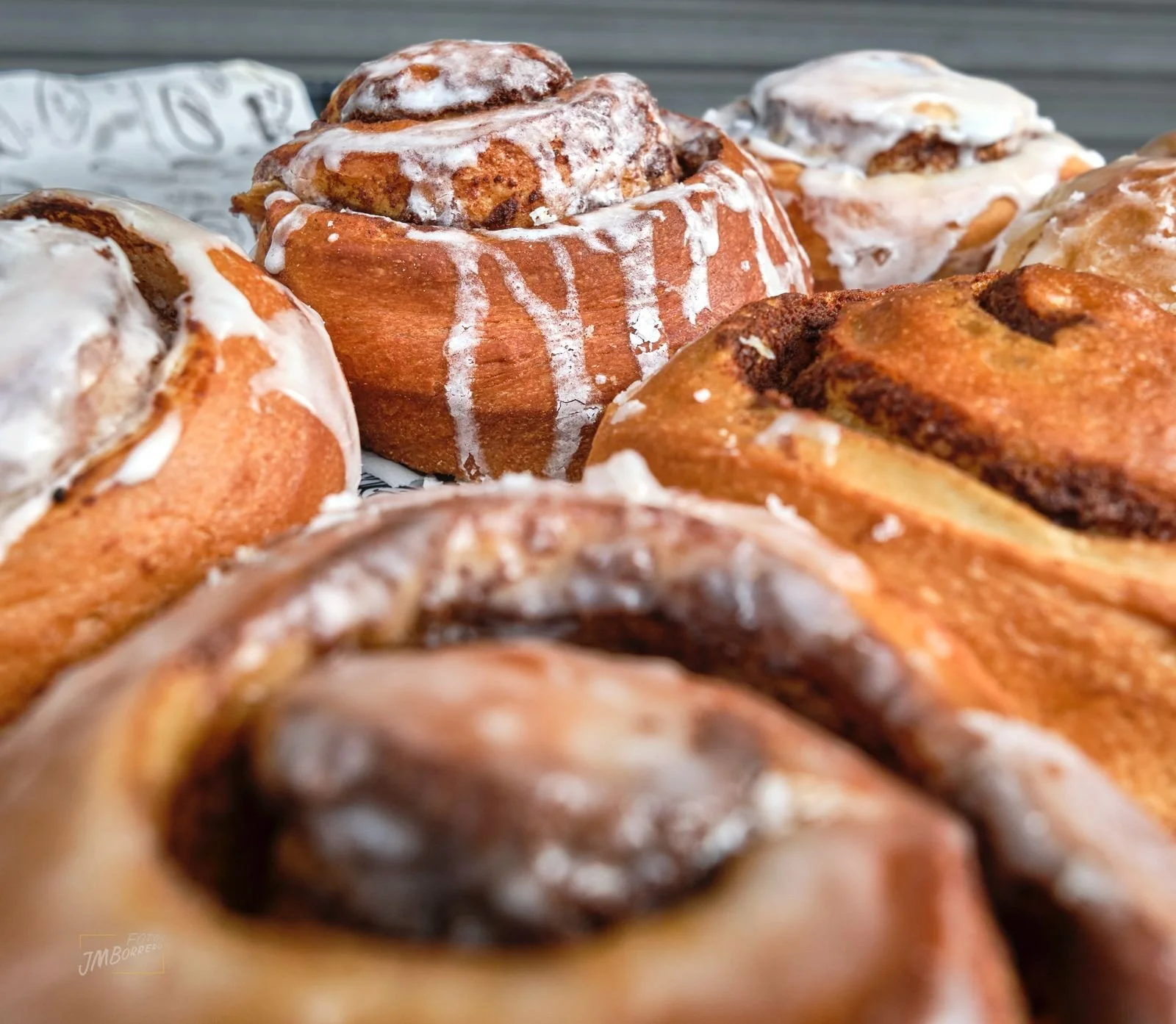 Close-up of a tray of freshly baked cinnamon rolls topped with white icing, showing their soft, flaky texture.
