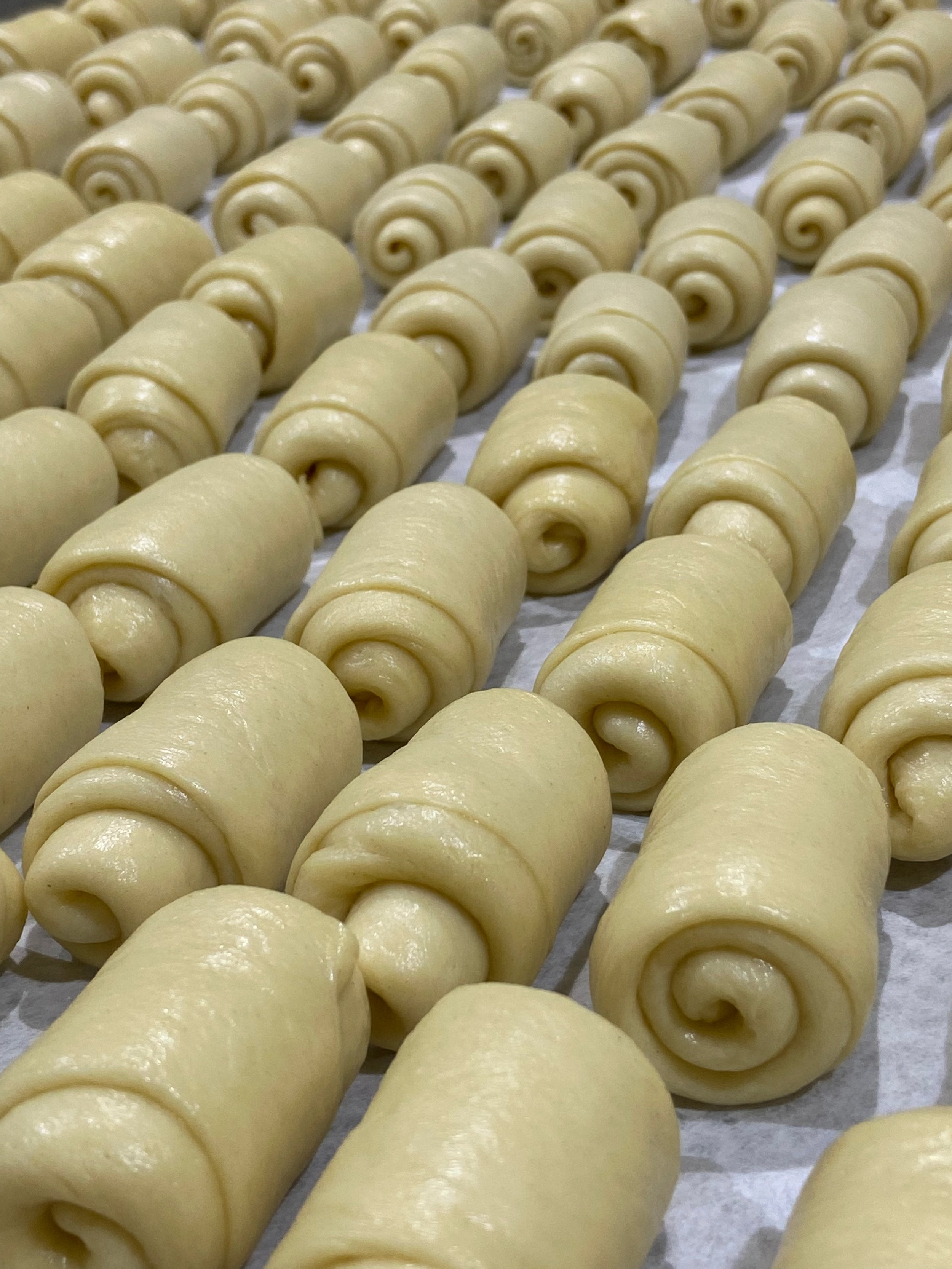 Raw croissants arranged in rows on a baking sheet lined with parchment paper.