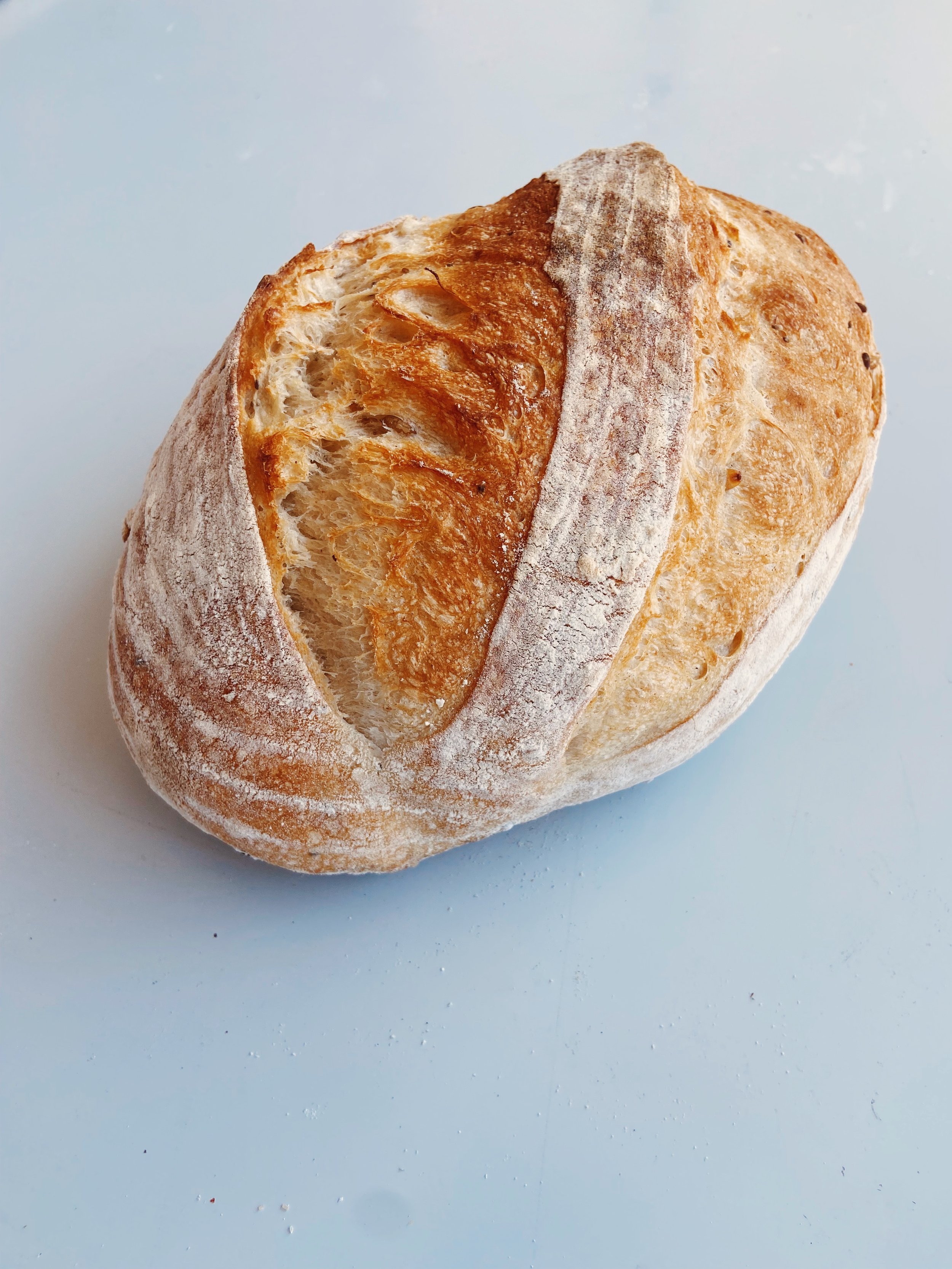 Fresh oval-shaped loaf of bread with a golden-brown crust on a white surface.