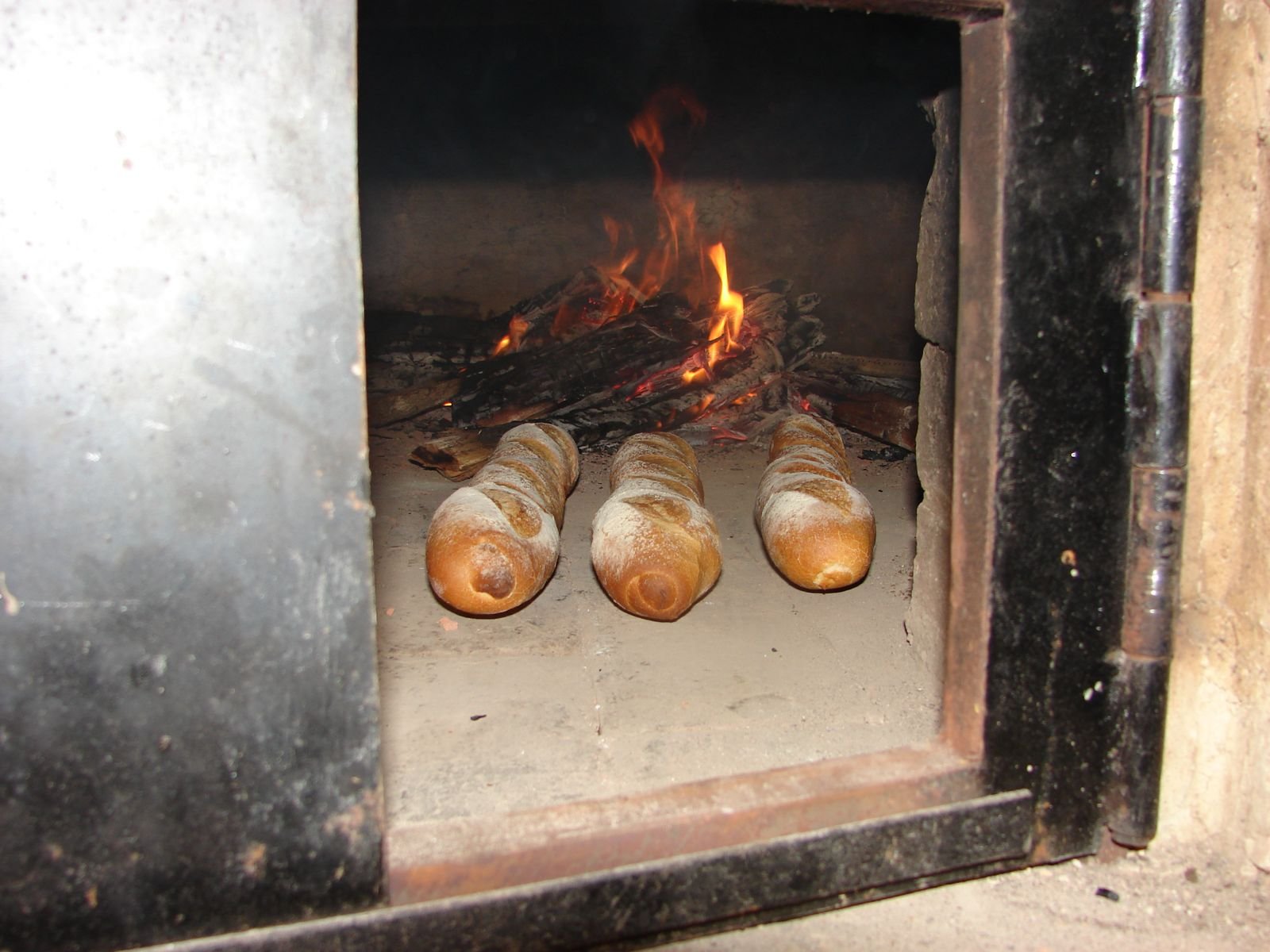 Four baguette loaves baking inside a brick oven with fire and glowing embers
