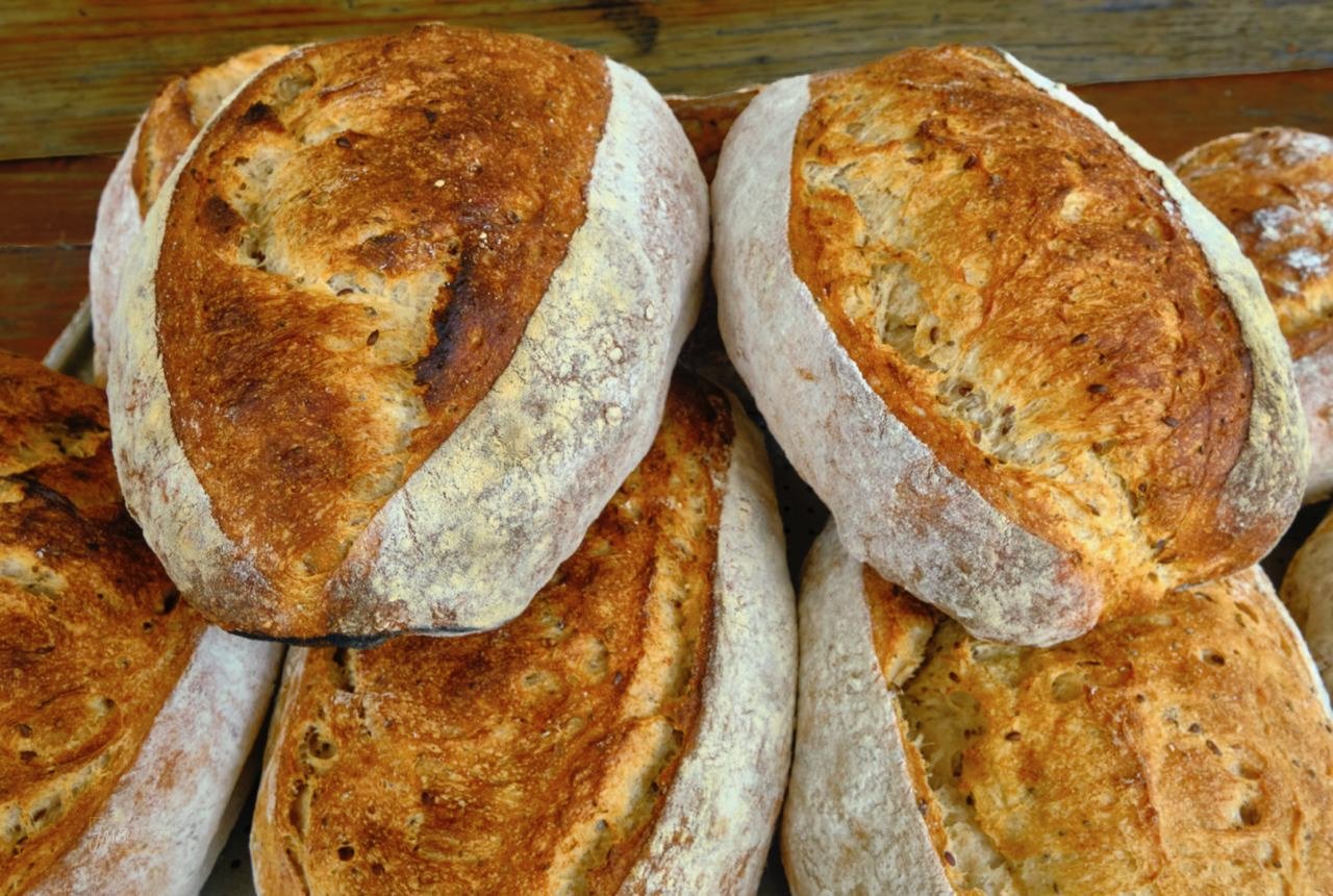 Close-up of several freshly baked sourdough bread loaves with a golden-brown crust and flour-dusted exterior.