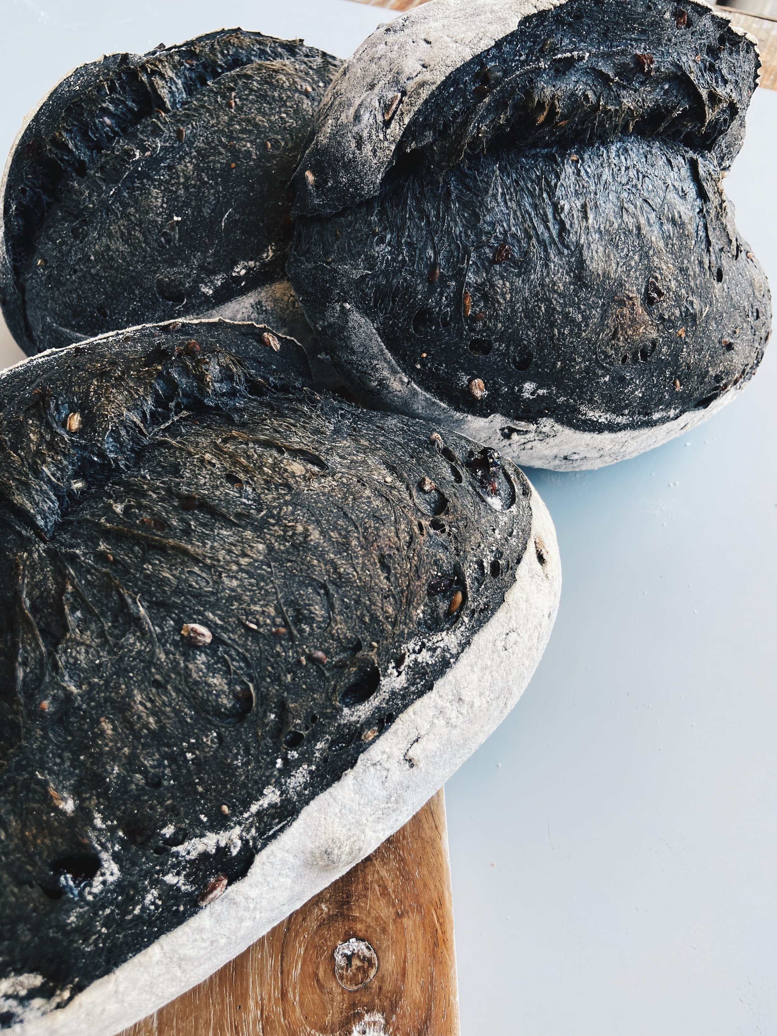 Three black bread loaves with seeds on a rustic wooden board.