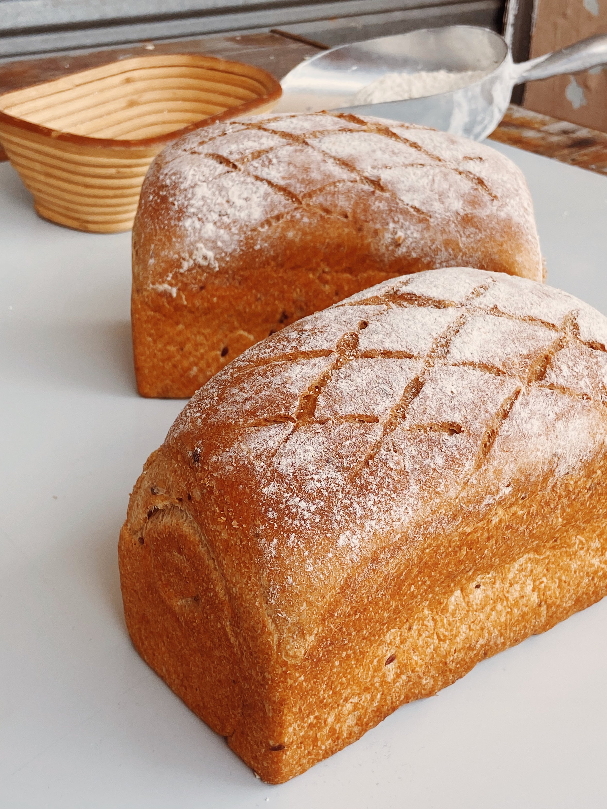 Two loaves of freshly baked bread with a golden crust and dusted with flour, placed on a white surface.