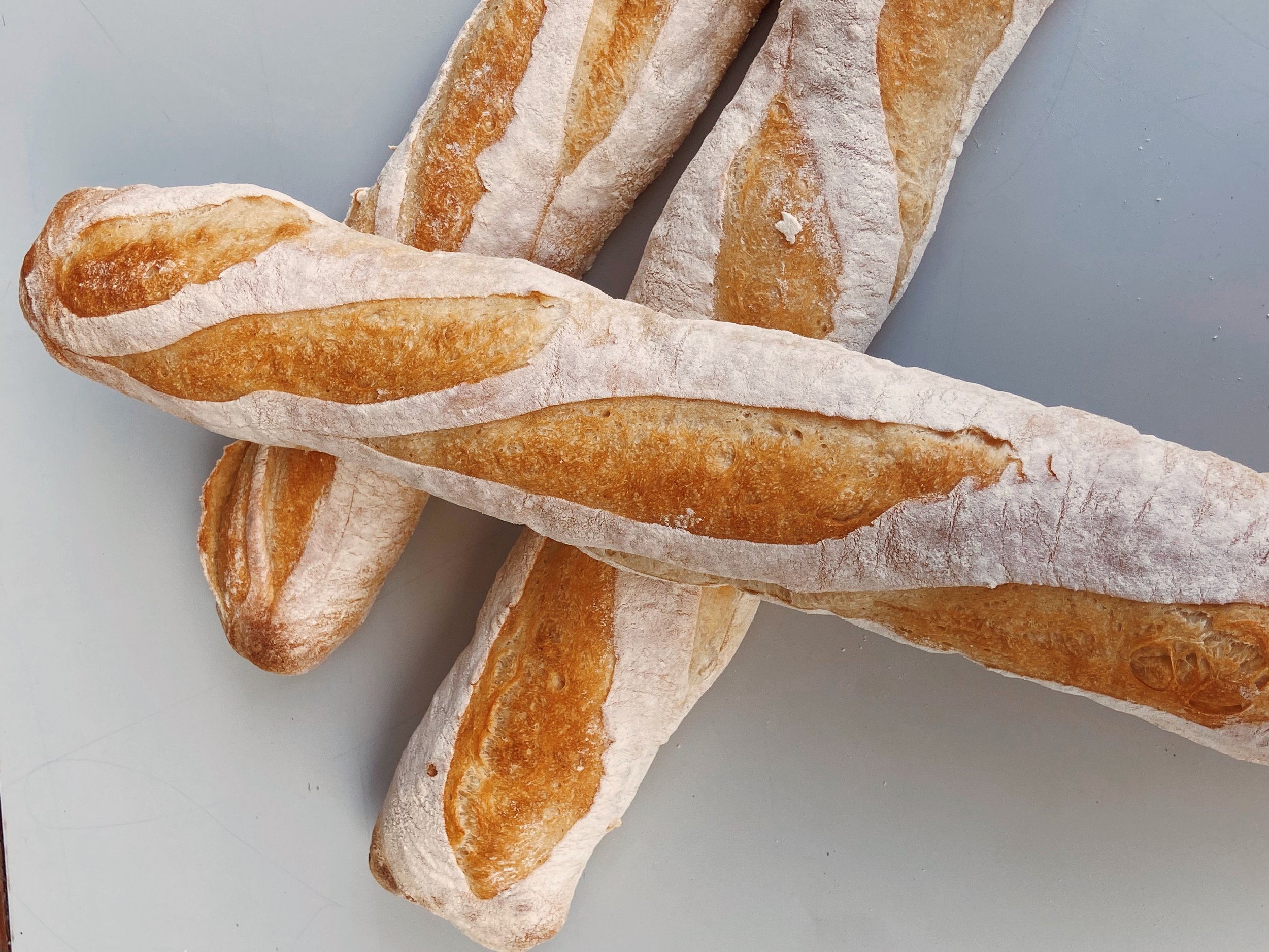 Several baked baguette loaves with a dusting of flour on a light gray surface.