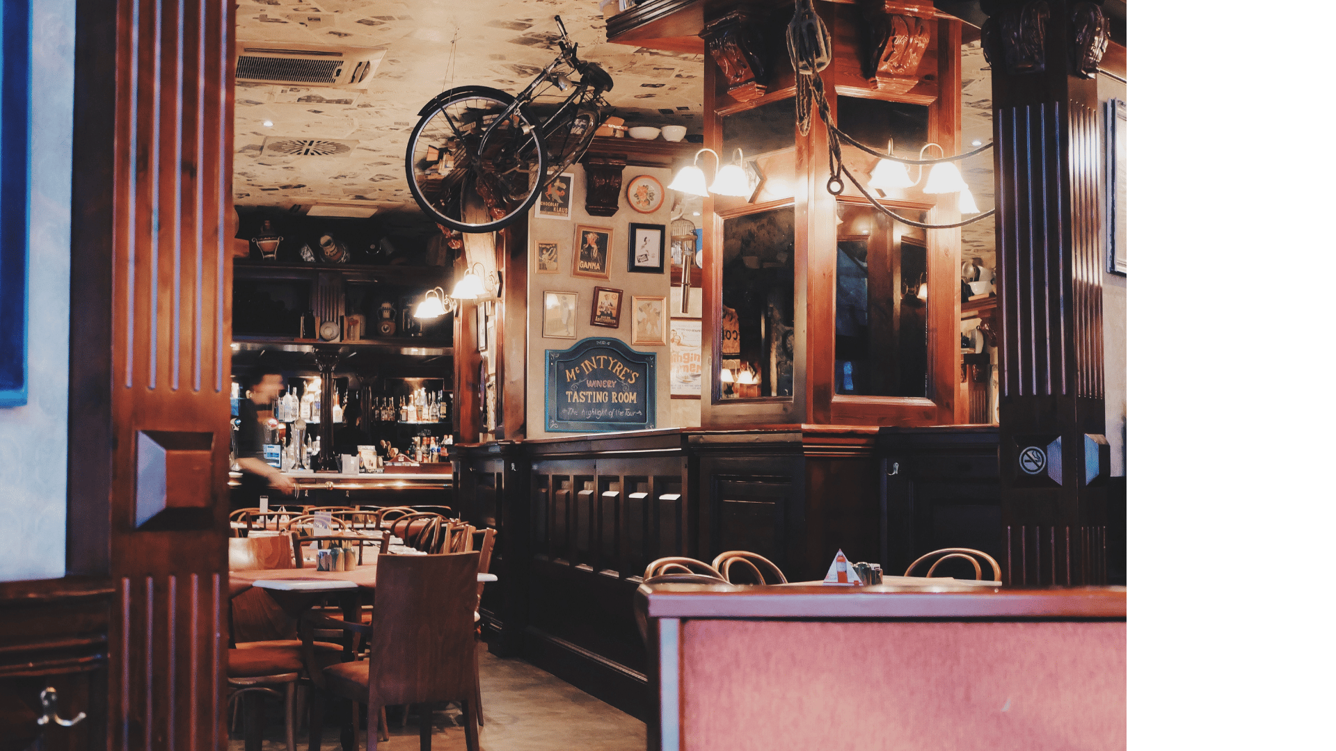 Interior of a cozy pub or restaurant with wooden decor, a bar area in the background, and pictures on the wall. A vintage bicycle is mounted upside down on the ceiling.