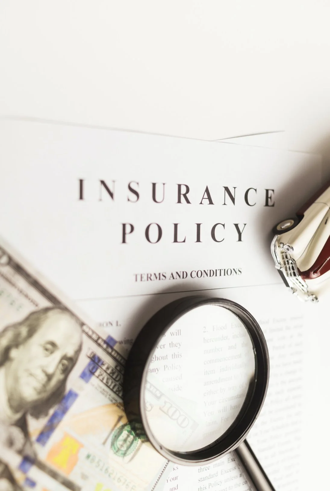 Insurance policy document with magnifying glass, hundred-dollar bill, and a set of keys.