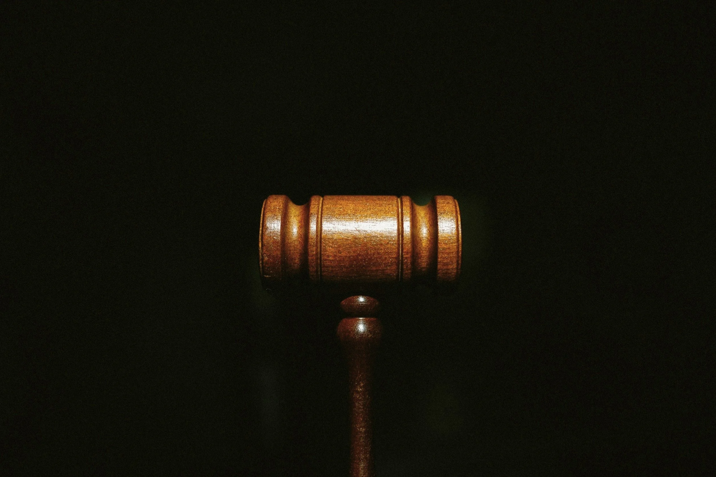 A wooden gavel resting on a sound block against a dark background.