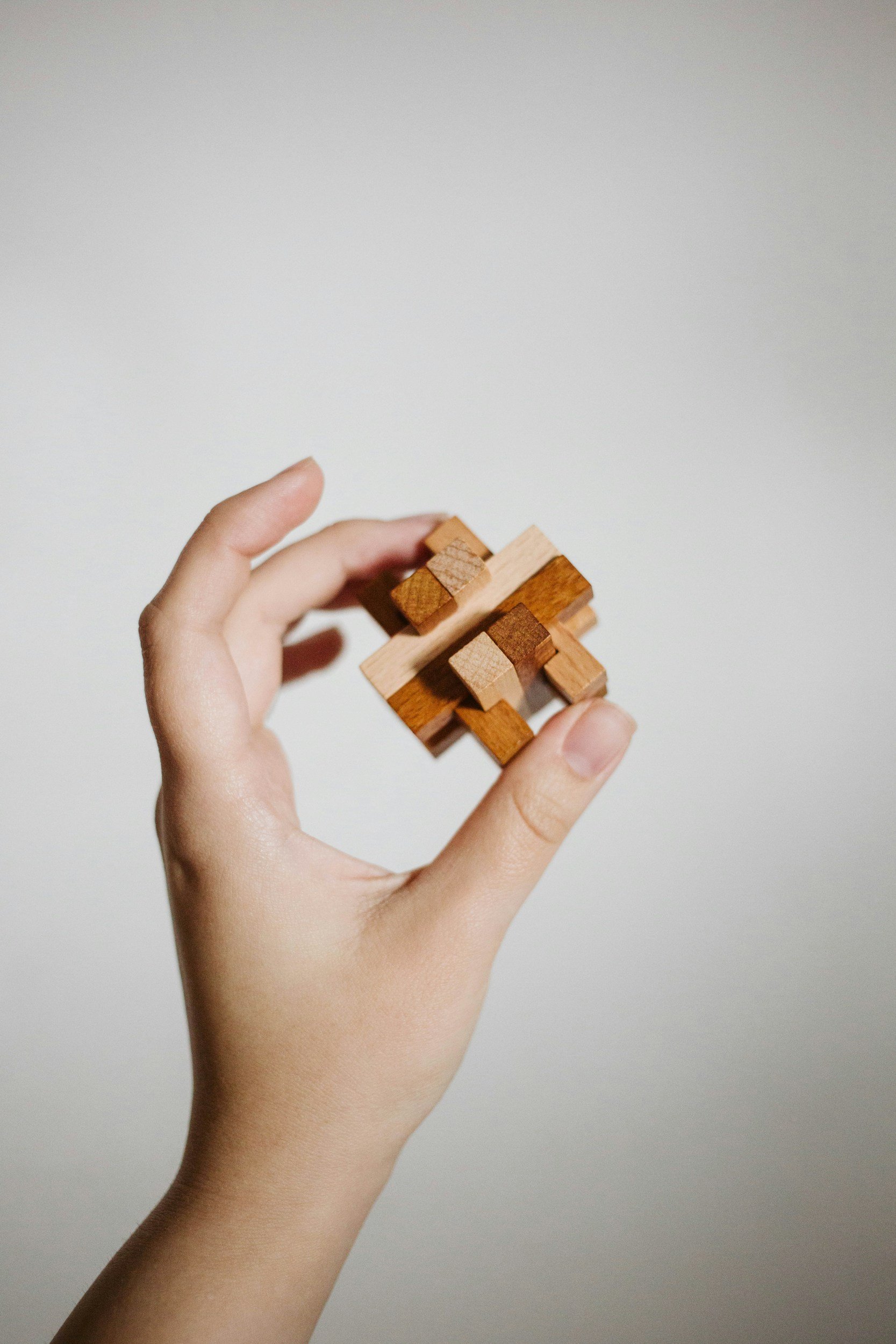 A person's hand holding a wooden puzzle with interlocking pieces against a plain background.