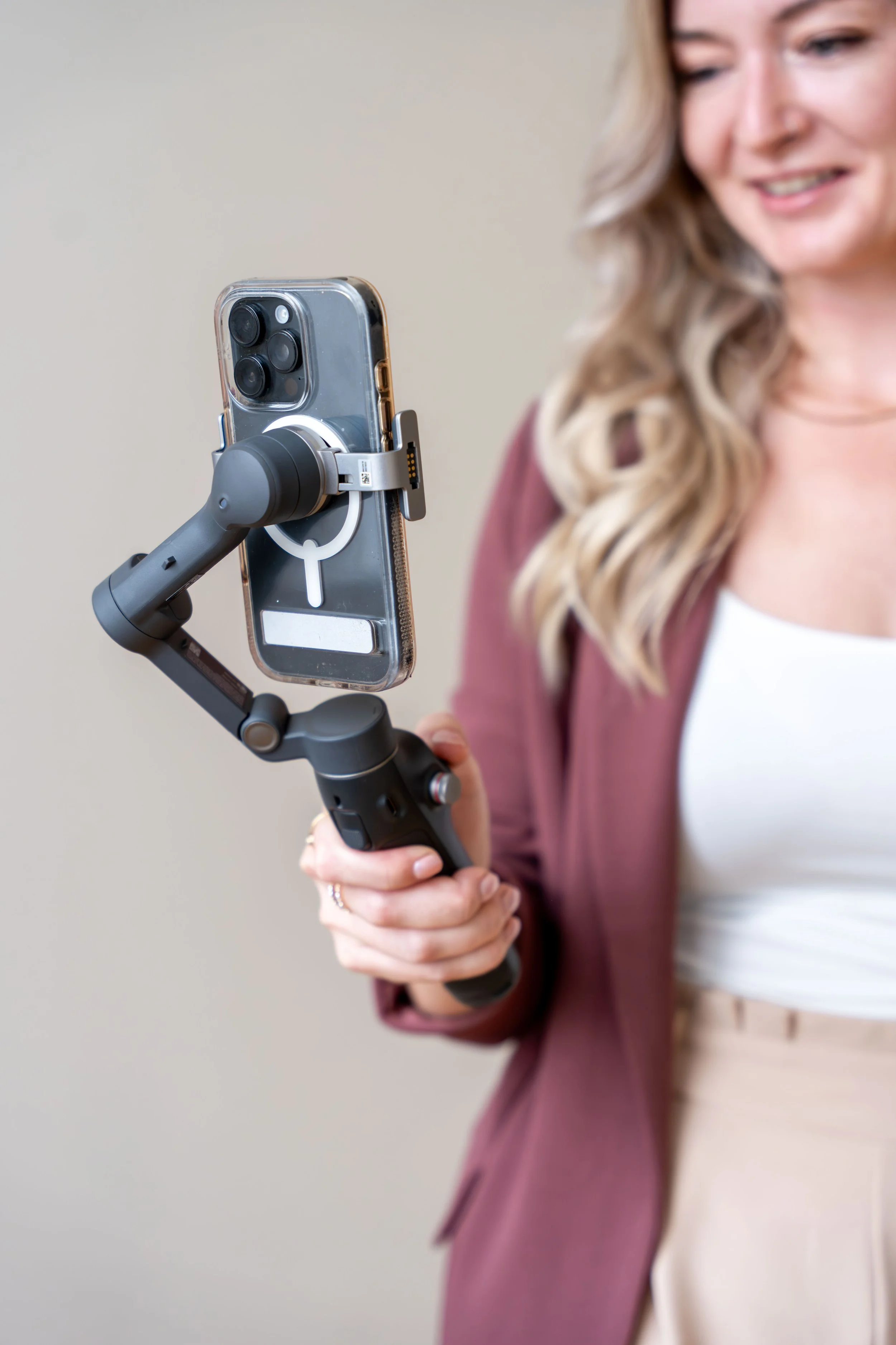 A woman holding a smartphone mounted on a handheld stabilizer or gimbal.