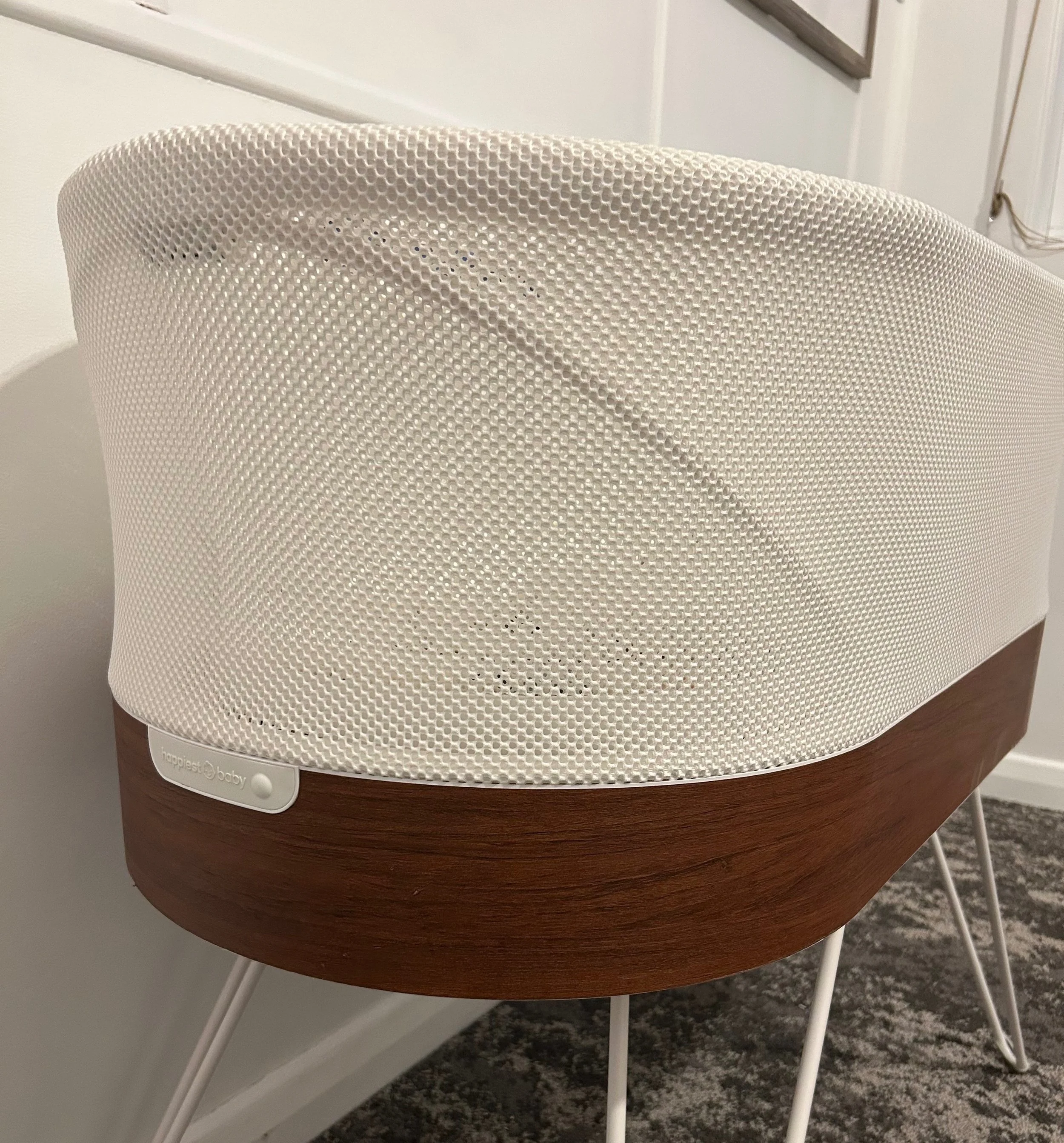 A white speaker with a perforated metal grille, mounted on a wooden base with white metal legs.