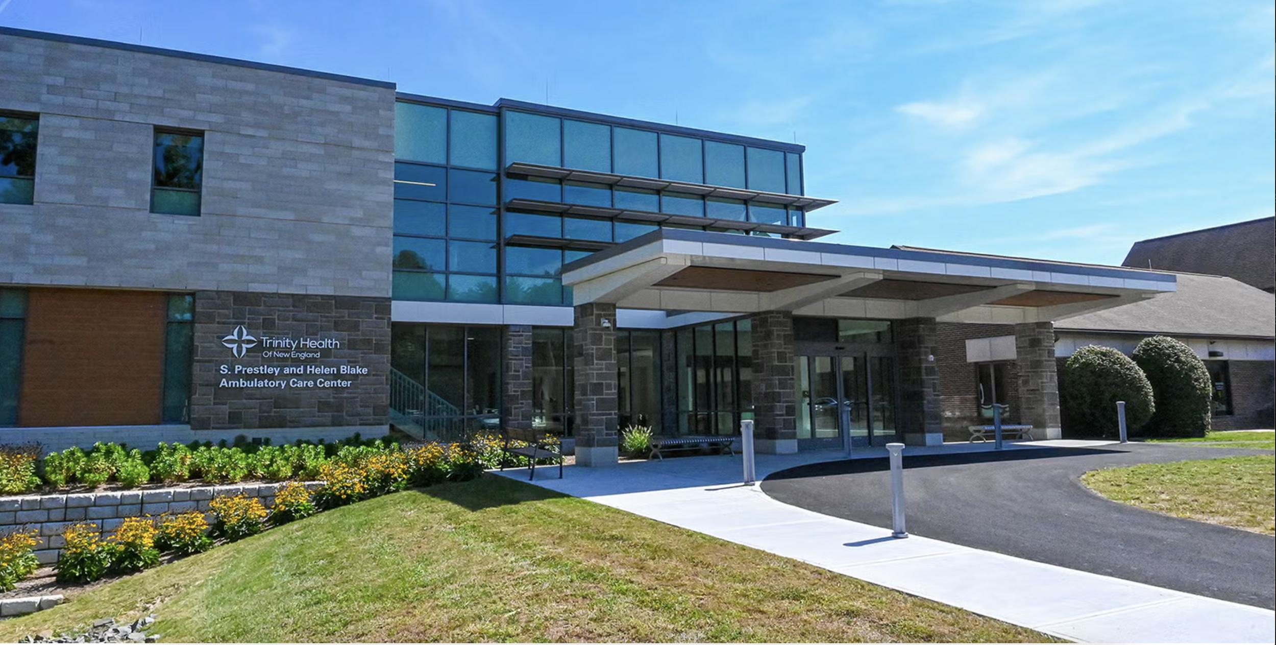 Exterior view of Trinity Health of New England S. Prestley and Helen Blake Ambulatory Care Center with a modern entrance, landscaped flowers, and a curved driveway.