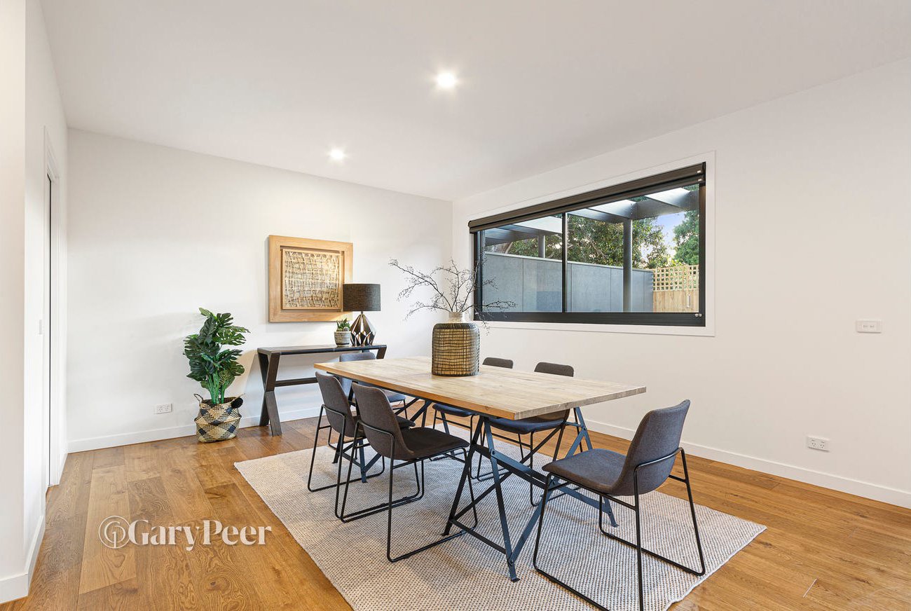 Modern dining room with wooden table, six black chairs, a window with a view of outdoor trees, a potted plant, and decorative items on a side table.