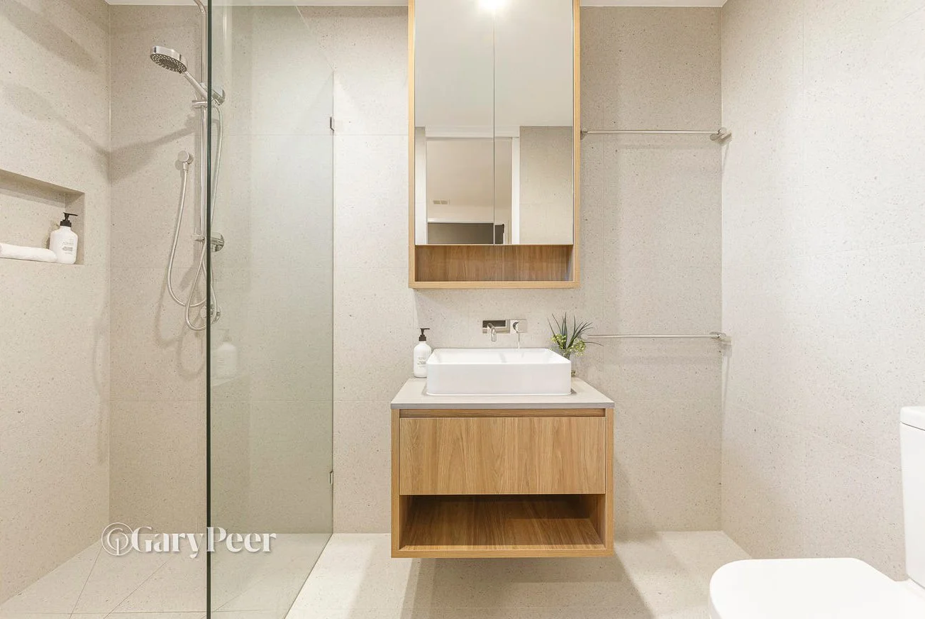 Modern bathroom with a walk-in shower, wooden vanity with a vessel sink, wall-mounted mirror, and a white toilet.