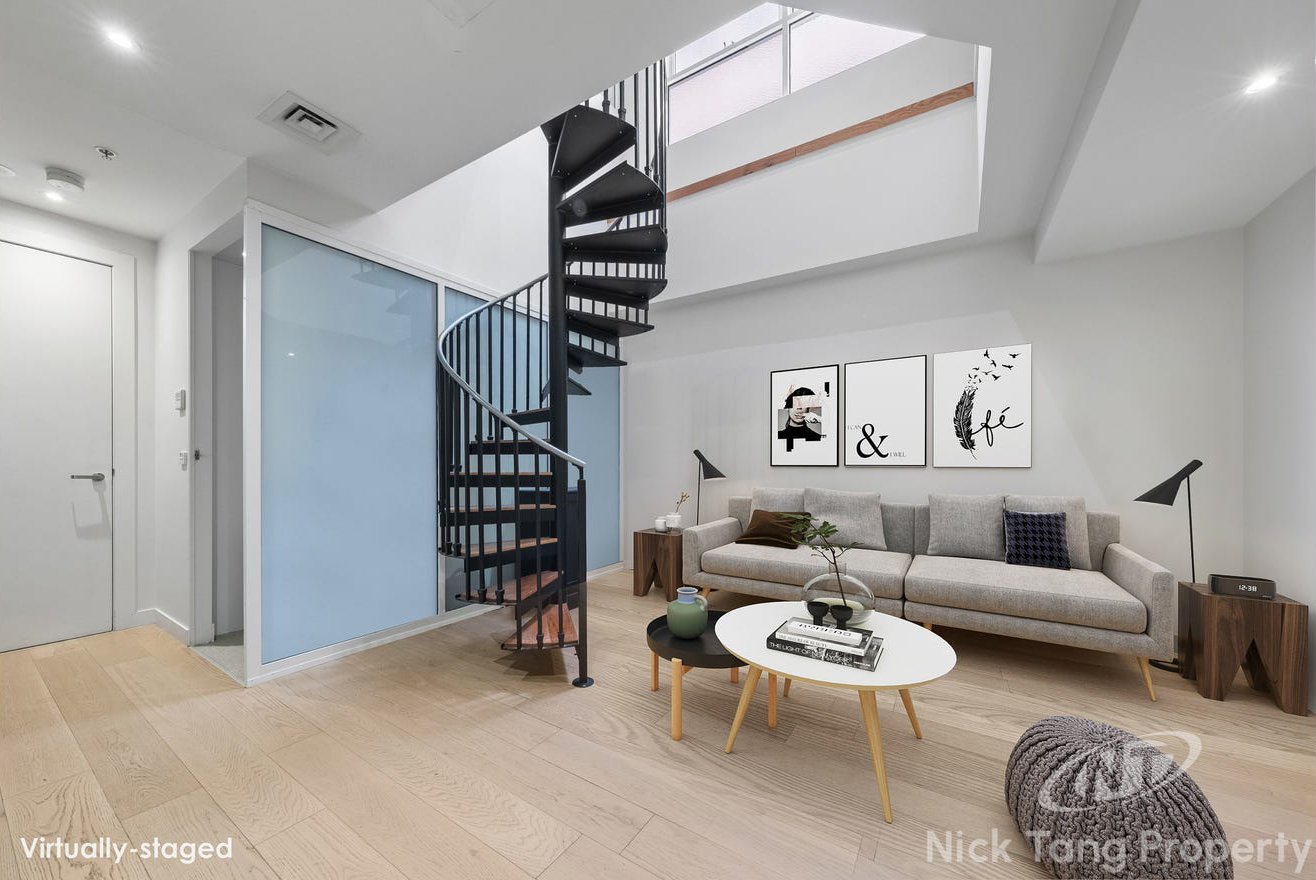Living room with a gray sofa, round and oval coffee tables, wall art, a spiral staircase, and wooden flooring.