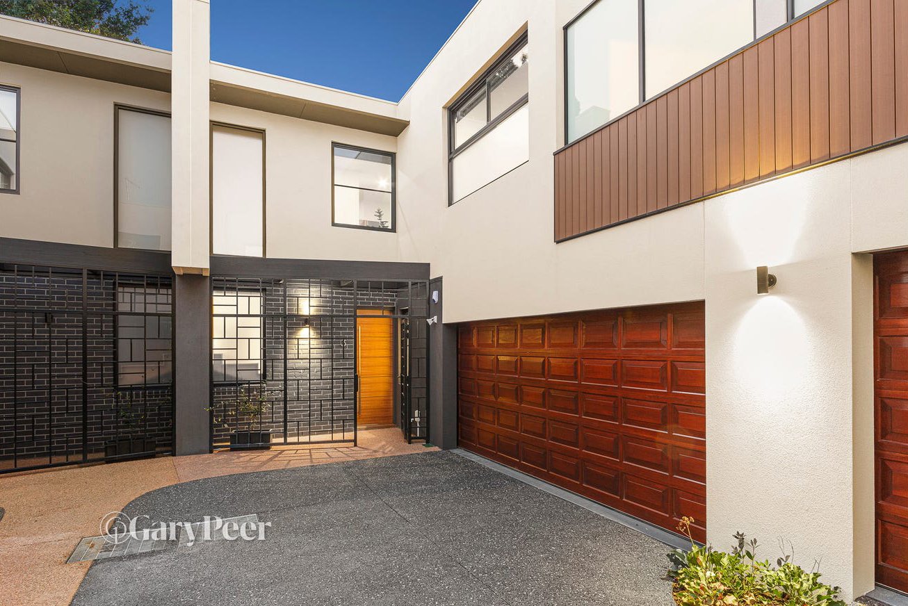 Modern residential building with a wooden garage door, a gated entryway, and a small garden in the foreground.