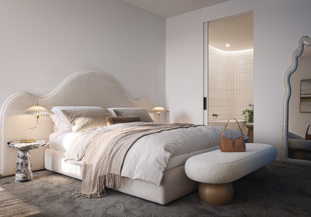 Modern bedroom with a large upholstered bed, beige headboard, and white bedding. Two gold bedside lamps, a textured side table, and a beige bench with a brown purse. An open sliding door reveals a white-tiled bathroom with a bathtub and a plant.
