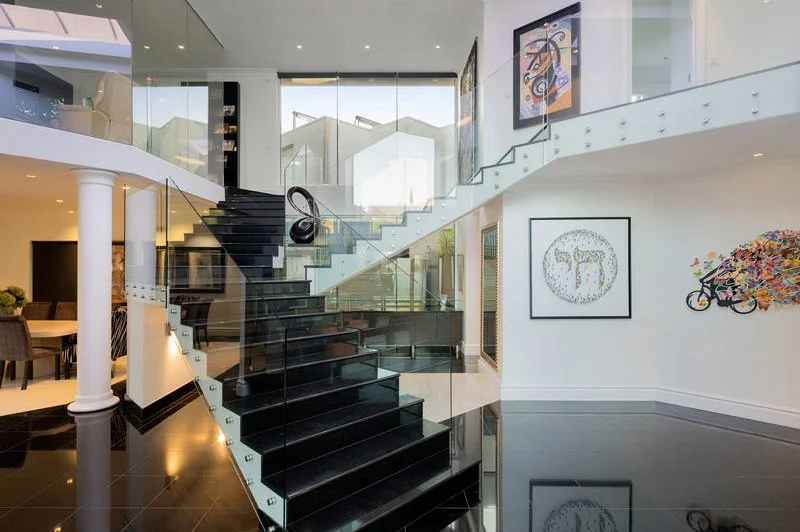 Modern interior with black staircase, glass railings, and contemporary artwork on white walls.